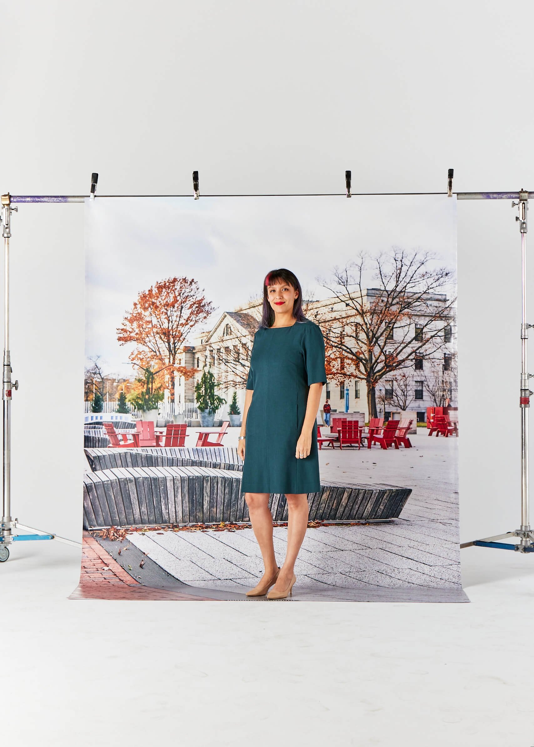 Woman standing in front of a large backdrop with a campus scene depicting red chairs and autumn trees.