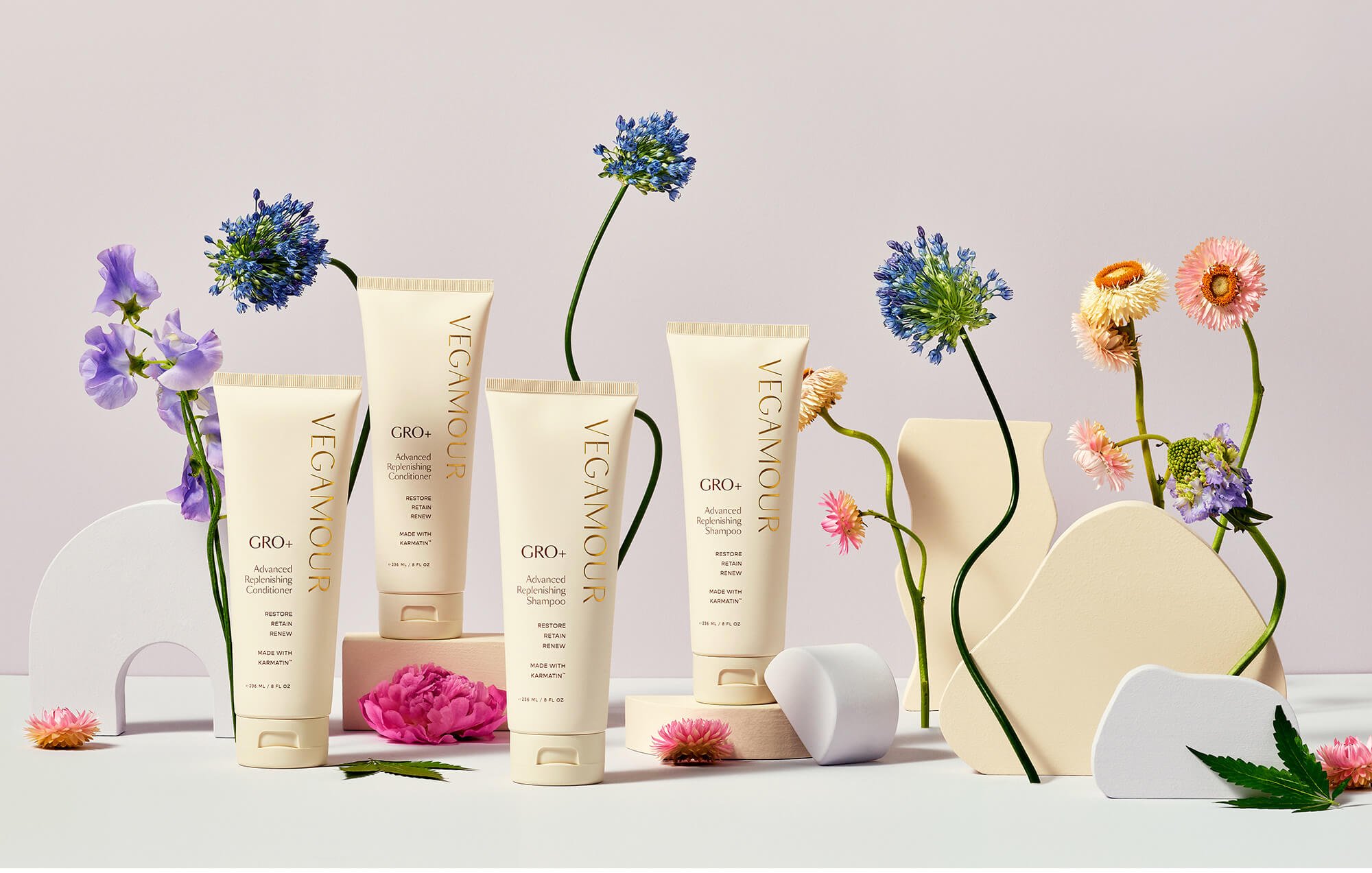 VEGAMOUR hair care products surrounded by colorful flowers and abstract shapes.