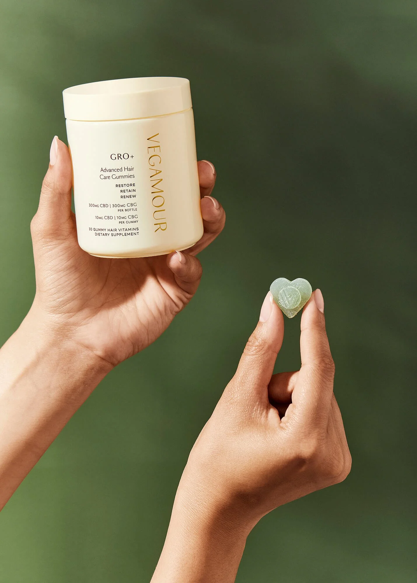 Hands holding a container and a heart-shaped gummy of Vegamour GRO+ Advanced Hair Care Gummies.