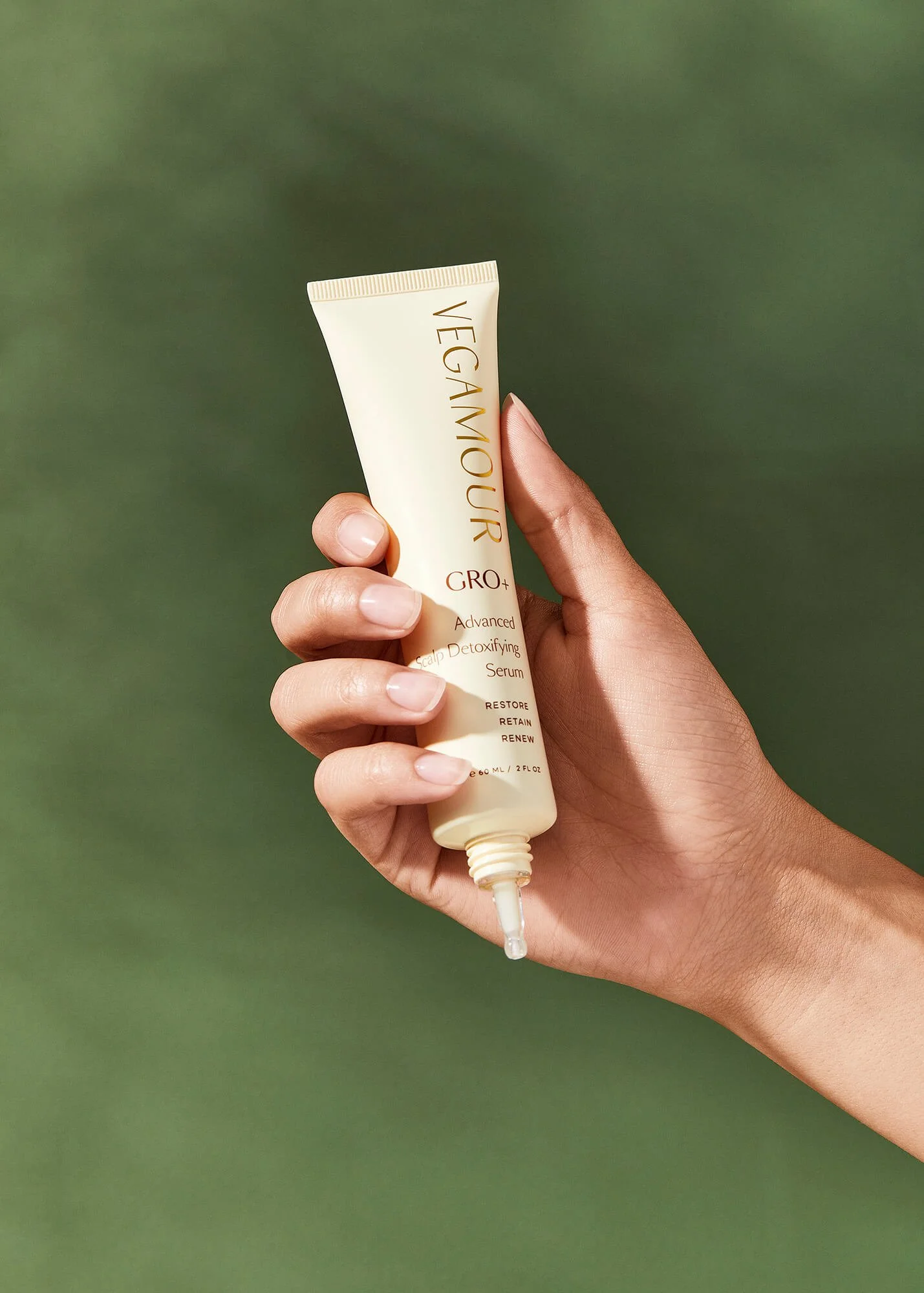 Person holding Vegamour GRO+ Advanced Scalp Detoxifying Serum in front of a green background.