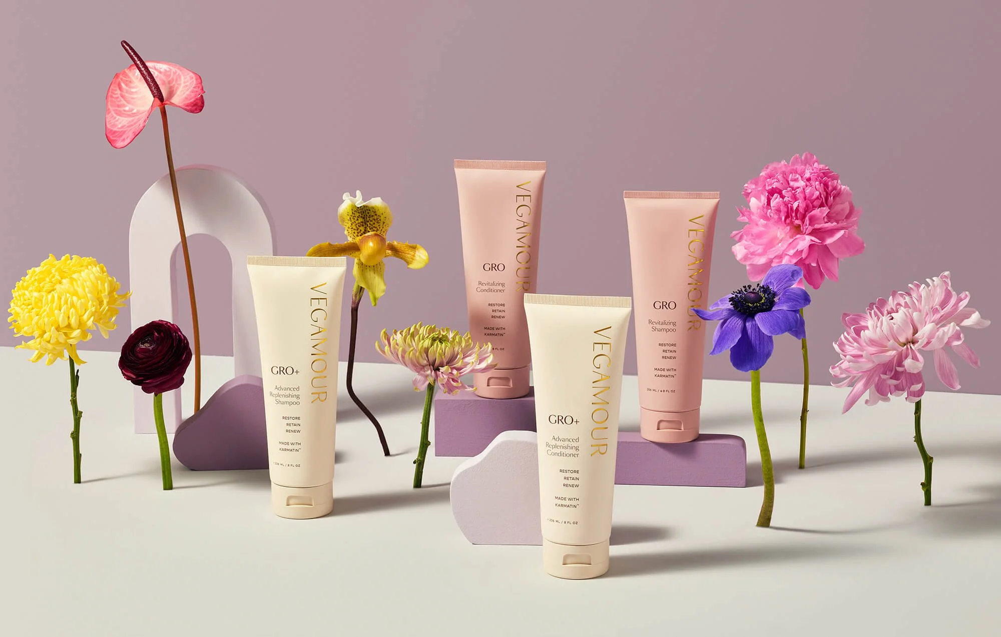 Vegamour hair care products surrounded by assorted colorful flowers against a purple background.