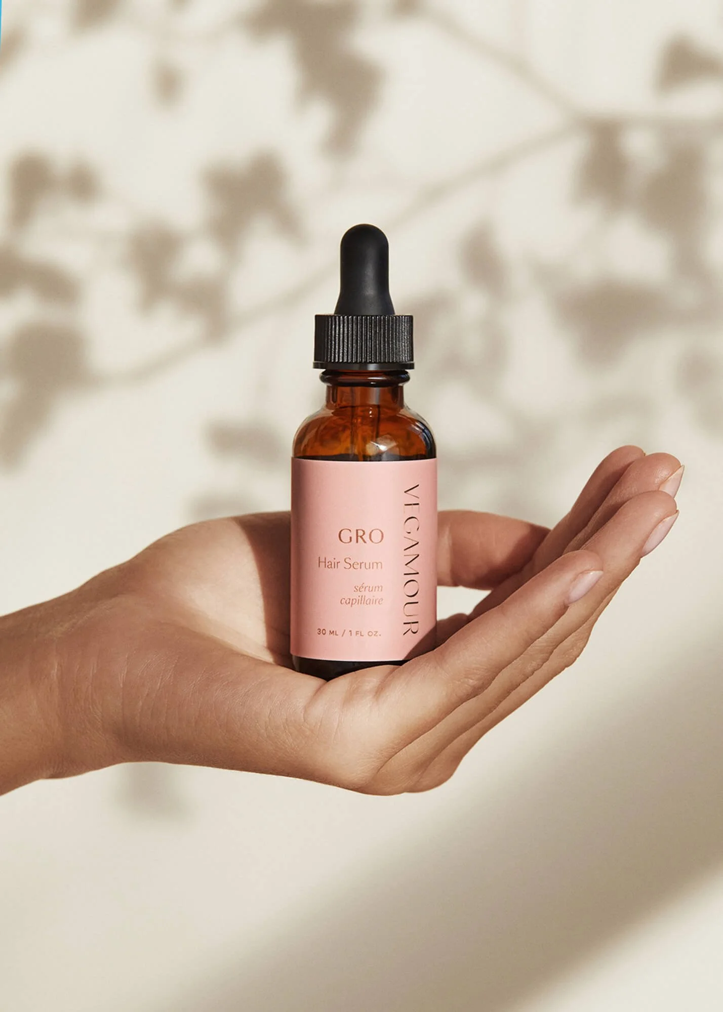 Hand holding Vegamour GRO Hair Serum with pink label and dropper top.