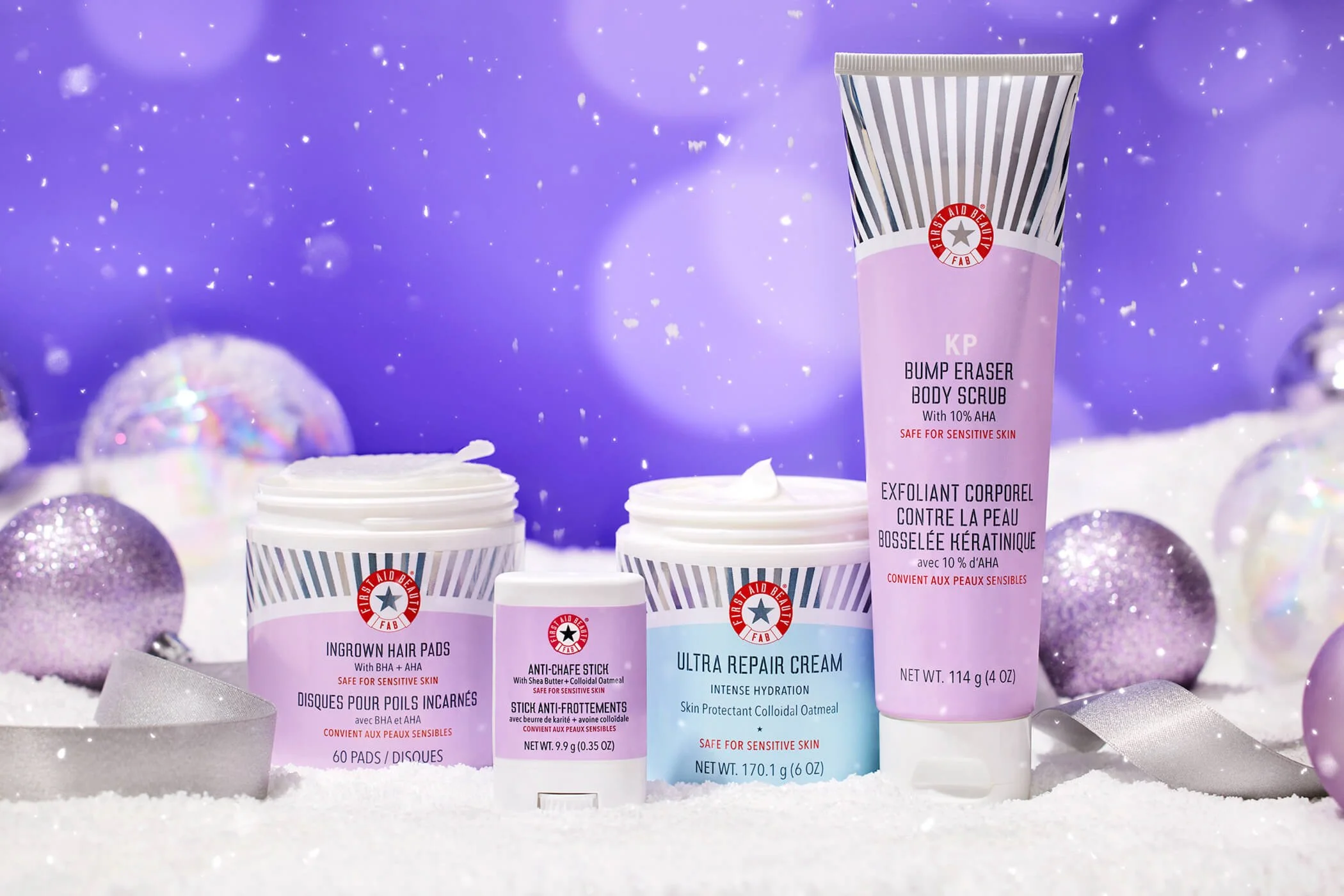 First Aid Beauty products, including ingrown hair pads, anti-chafe stick, ultra repair cream, and KP bump eraser body scrub, surrounded by snow and ornaments on a purple background.