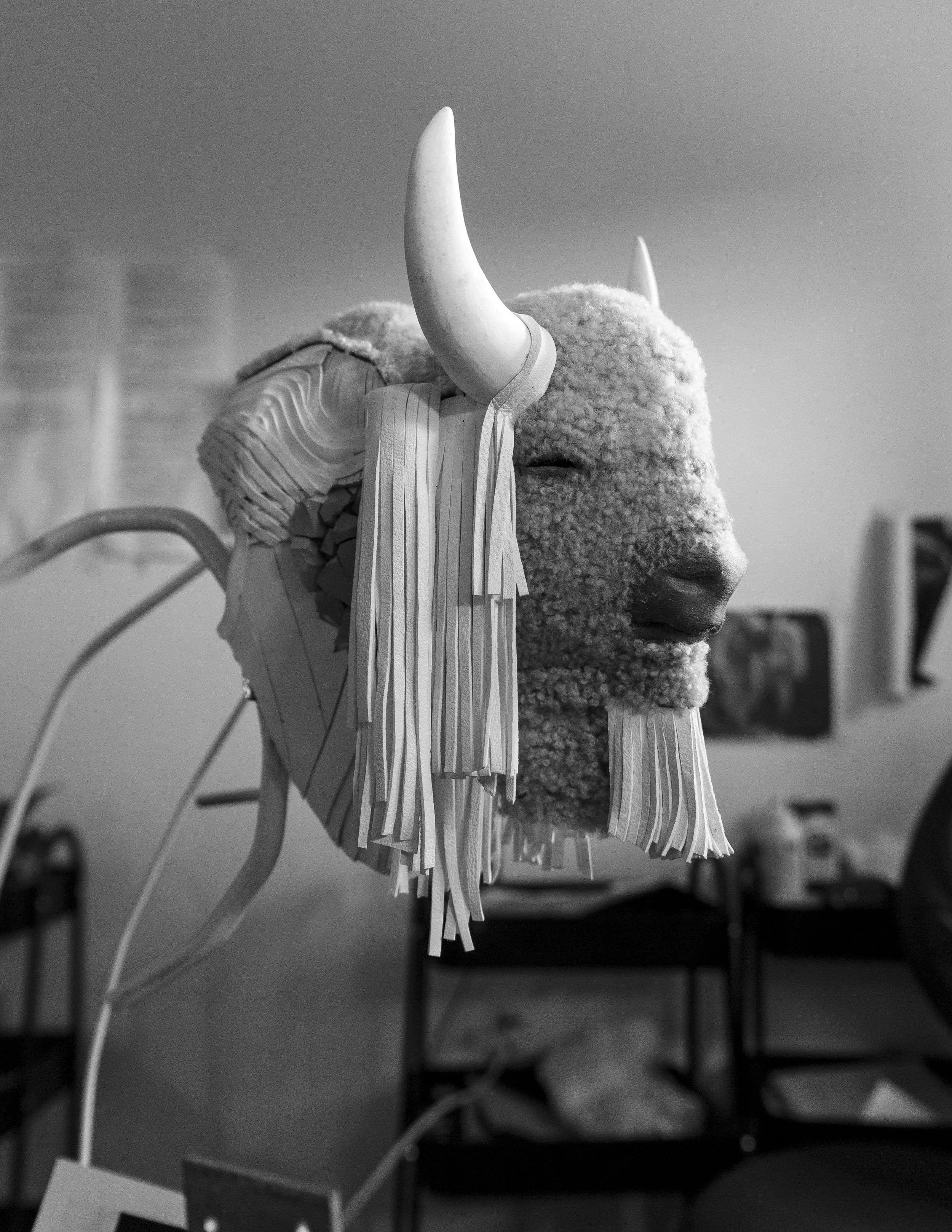 Black and white image of a bison head sculpture with horns and fringe details.