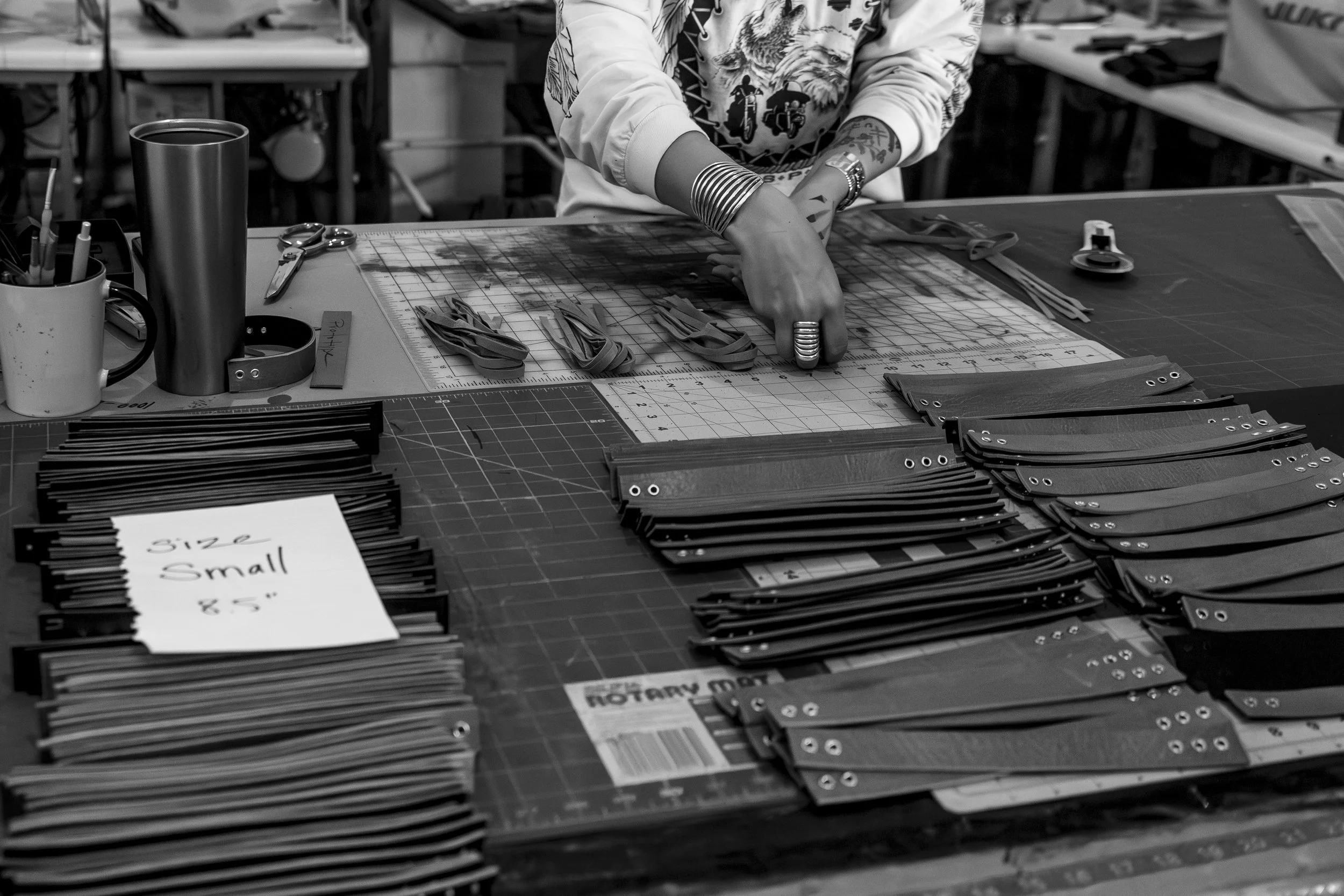 Person organizing pieces of leather on a work table in a workshop, with stacks of labeled small size leather strips and tools in the background.