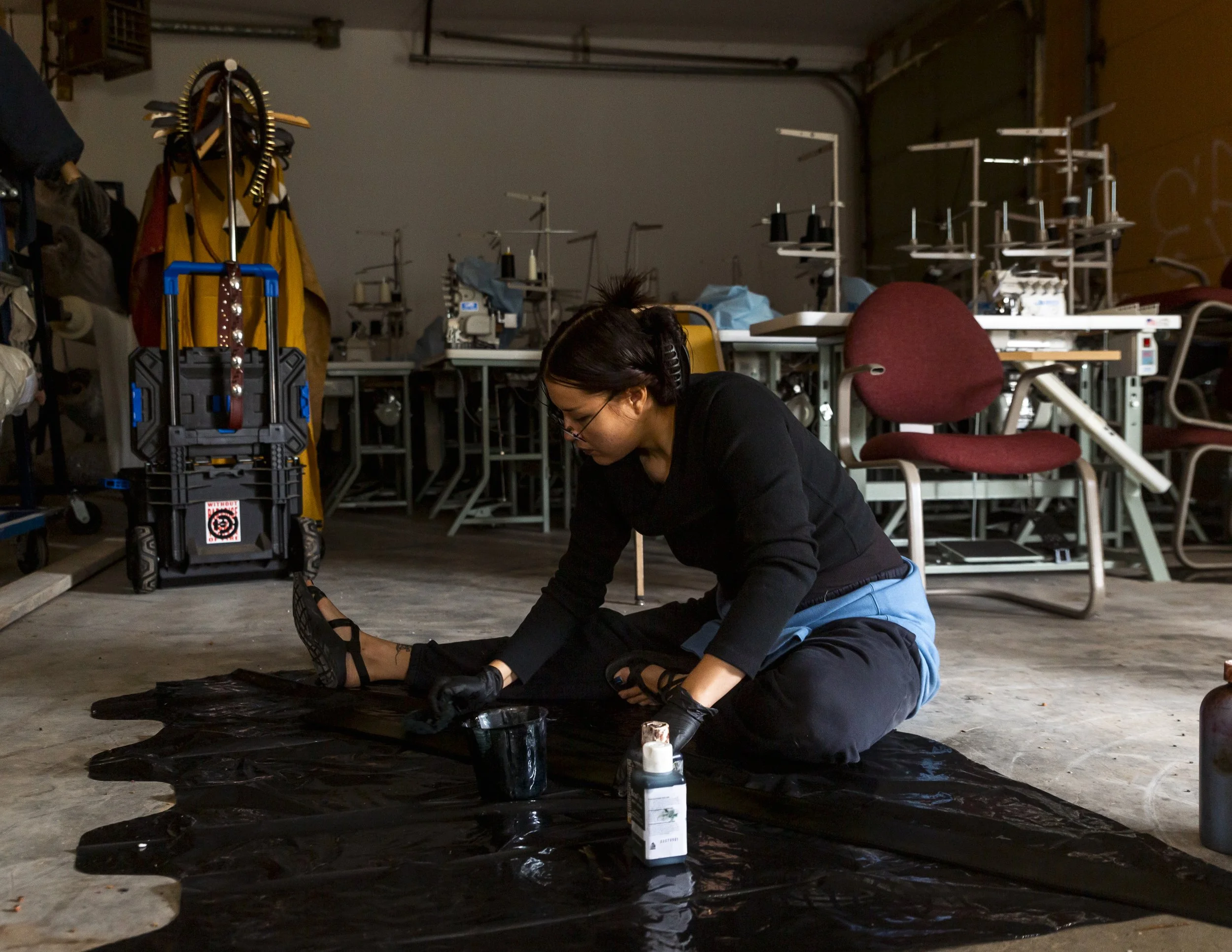 Person working on a black fabric in a workshop, surrounded by sewing machines and equipment.