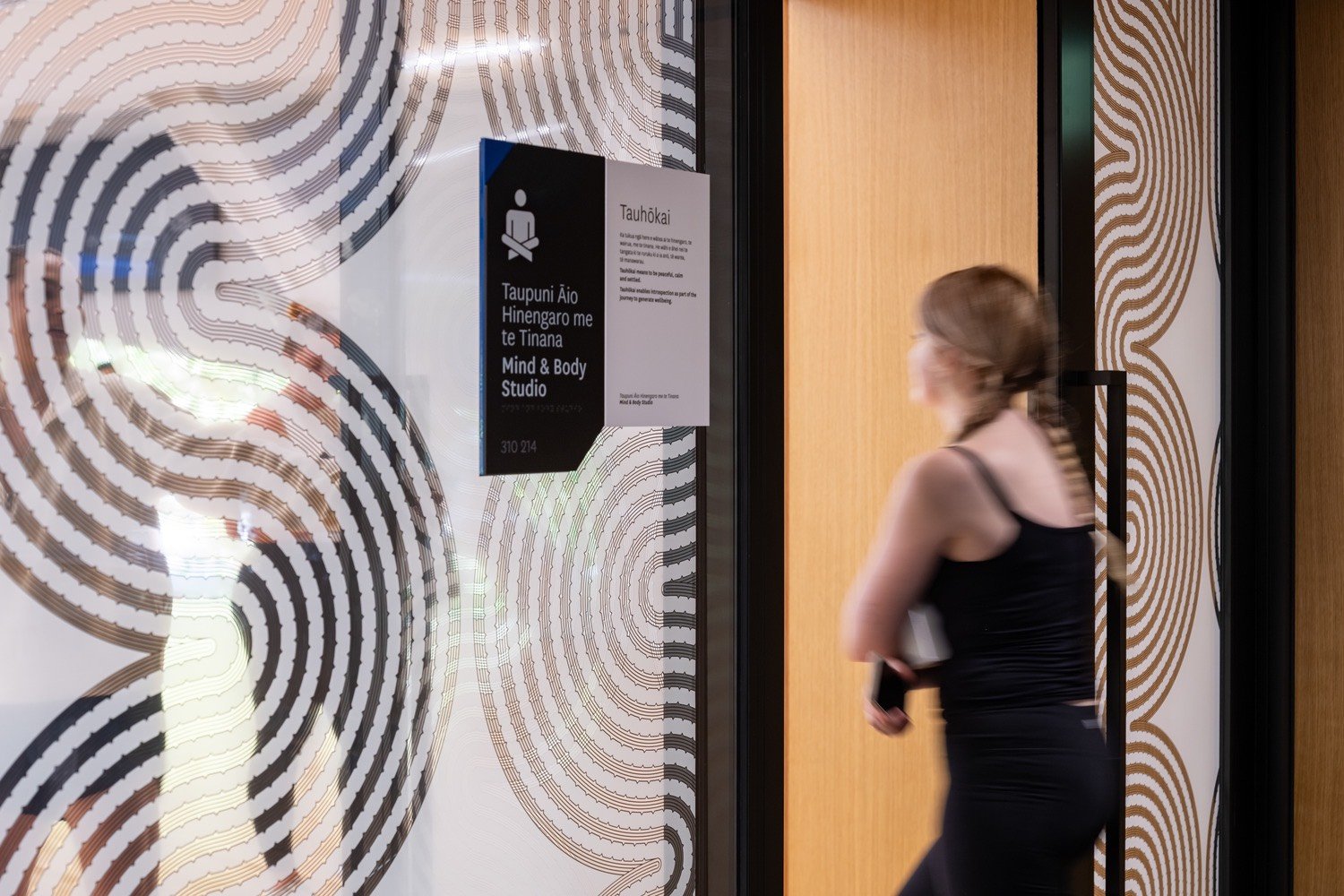 A woman walking into a fitness studio, past a large glass wall with a patterned privacy screen, representing experiential projects