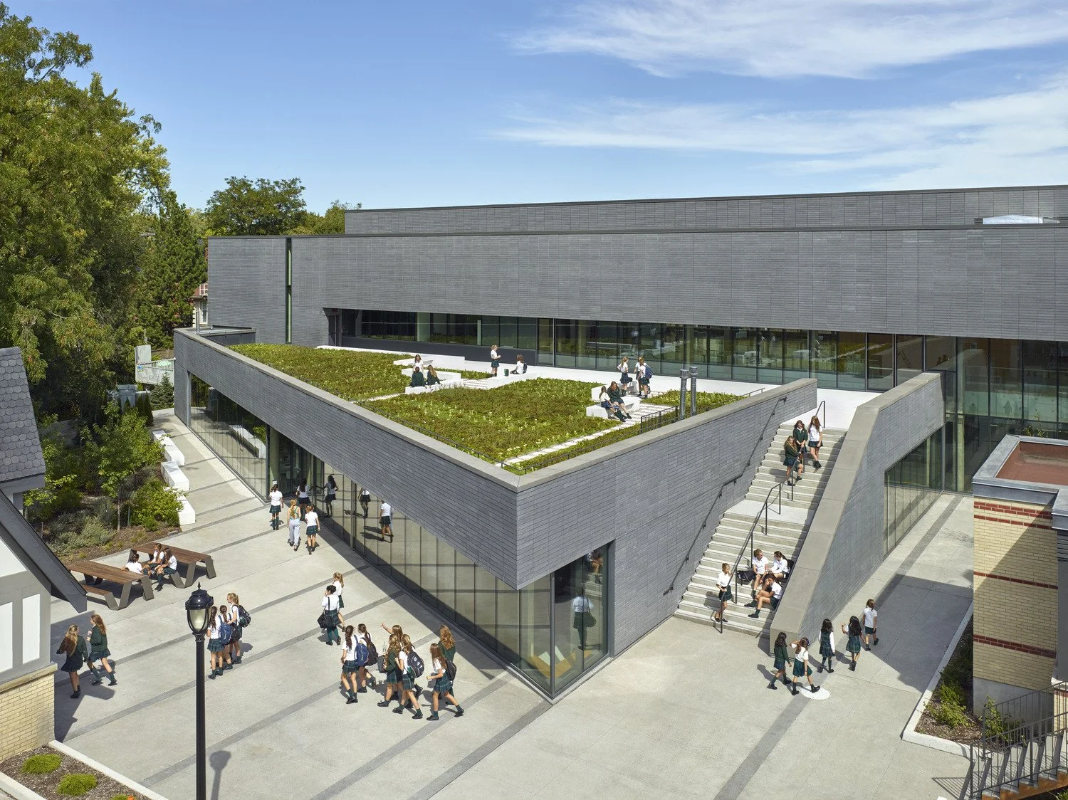 A modern school building with a rooftop garden where students are sitting and walking, and outdoor stairs leading to the upper level.