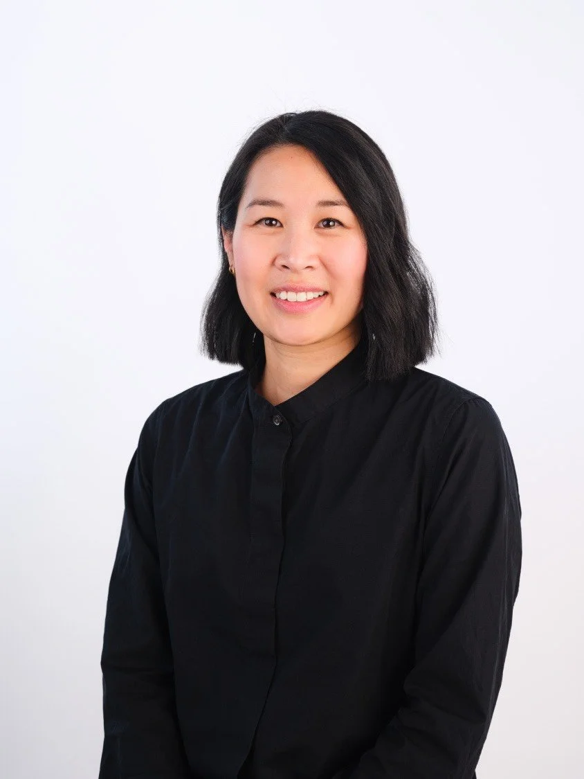 Headshot of a woman with shoulder-length black hair wearing a black button-up shirt, smiling against a plain white background.
