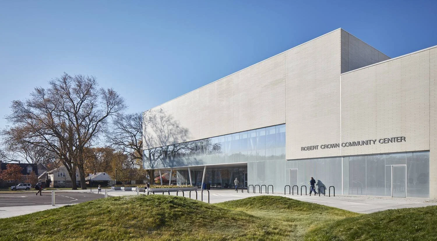 Exterior view of the Robert Crown Community Center with a modern architectural design, large glass windows, and a landscaped foreground, under a clear blue sky.