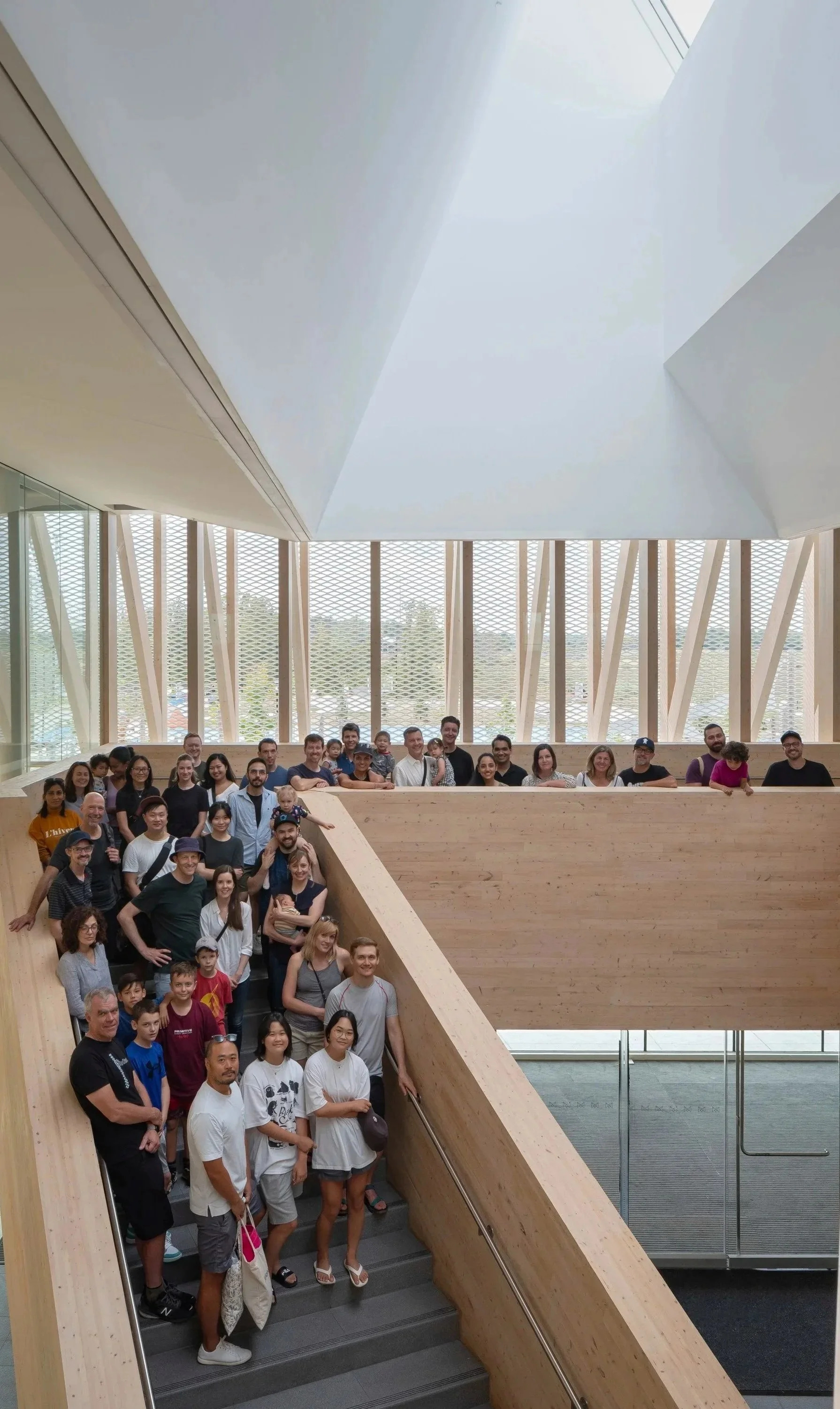 Group of diverse people posing on a staircase inside a modern building with large windows and wooden architectural features.
