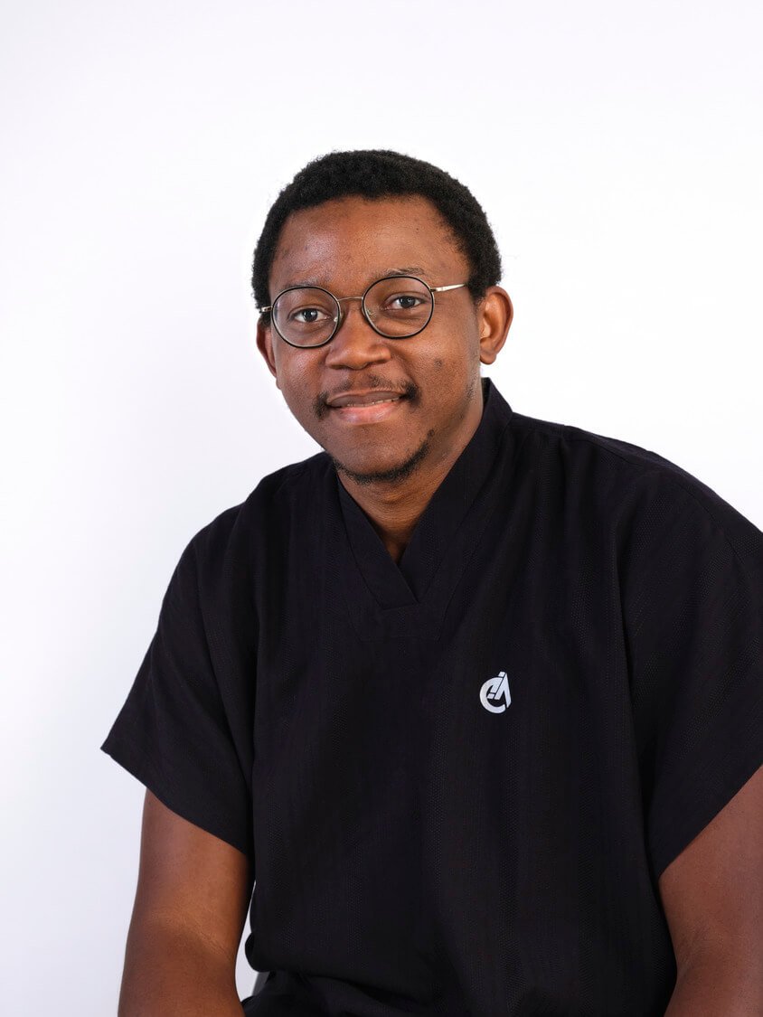 Headshot of a man with short curly black hair and glasses wearing a black shirt with a small logo on the chest, sitting against a white background.