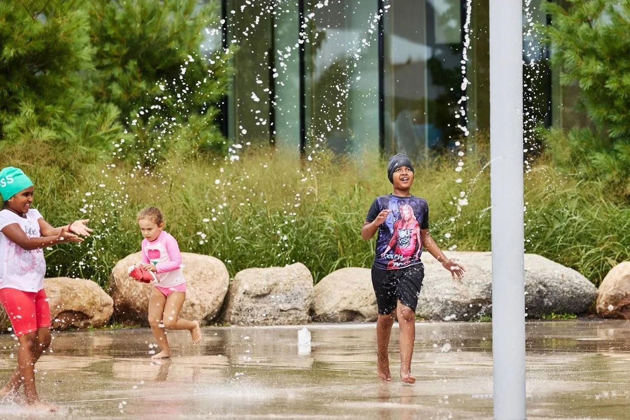 Children playing and running through a splash pad outdoors, representing landscape projects