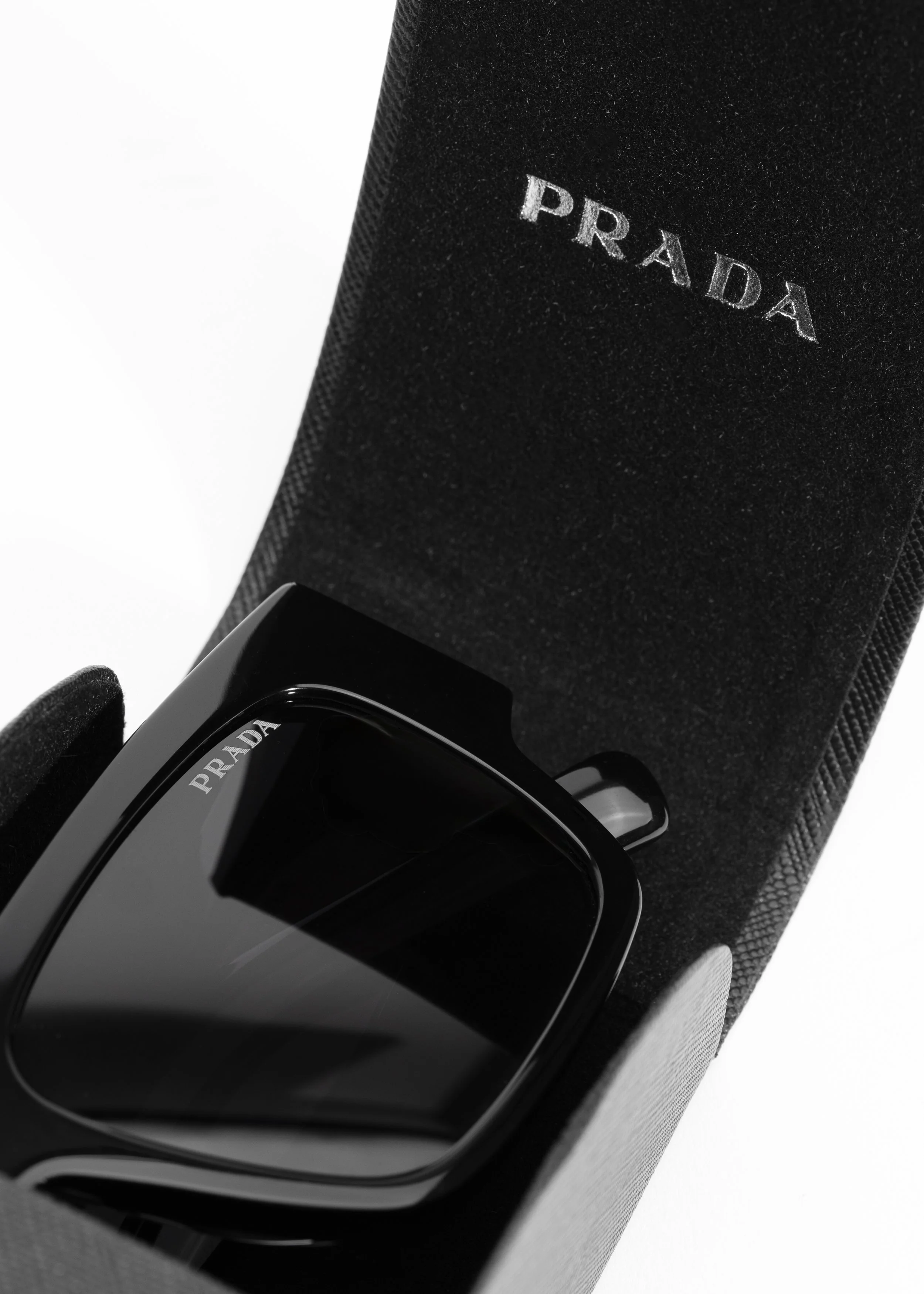 Close-up of a black Prada sunglasses case with the Prada logo, partially opened to show a pair of black Prada sunglasses inside.