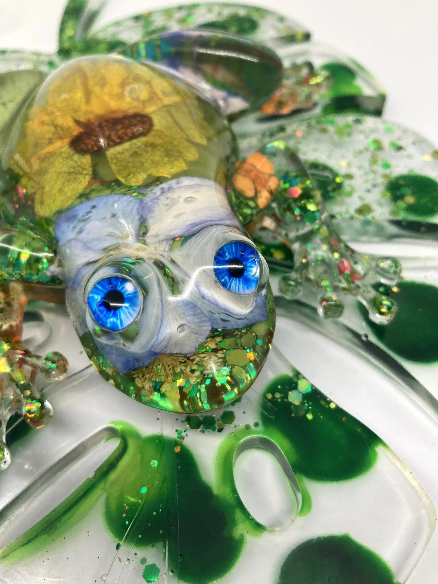 Close-up of a colorful resin sculpture resembling a chameleon with detailed eyes, standing on a green leaf.