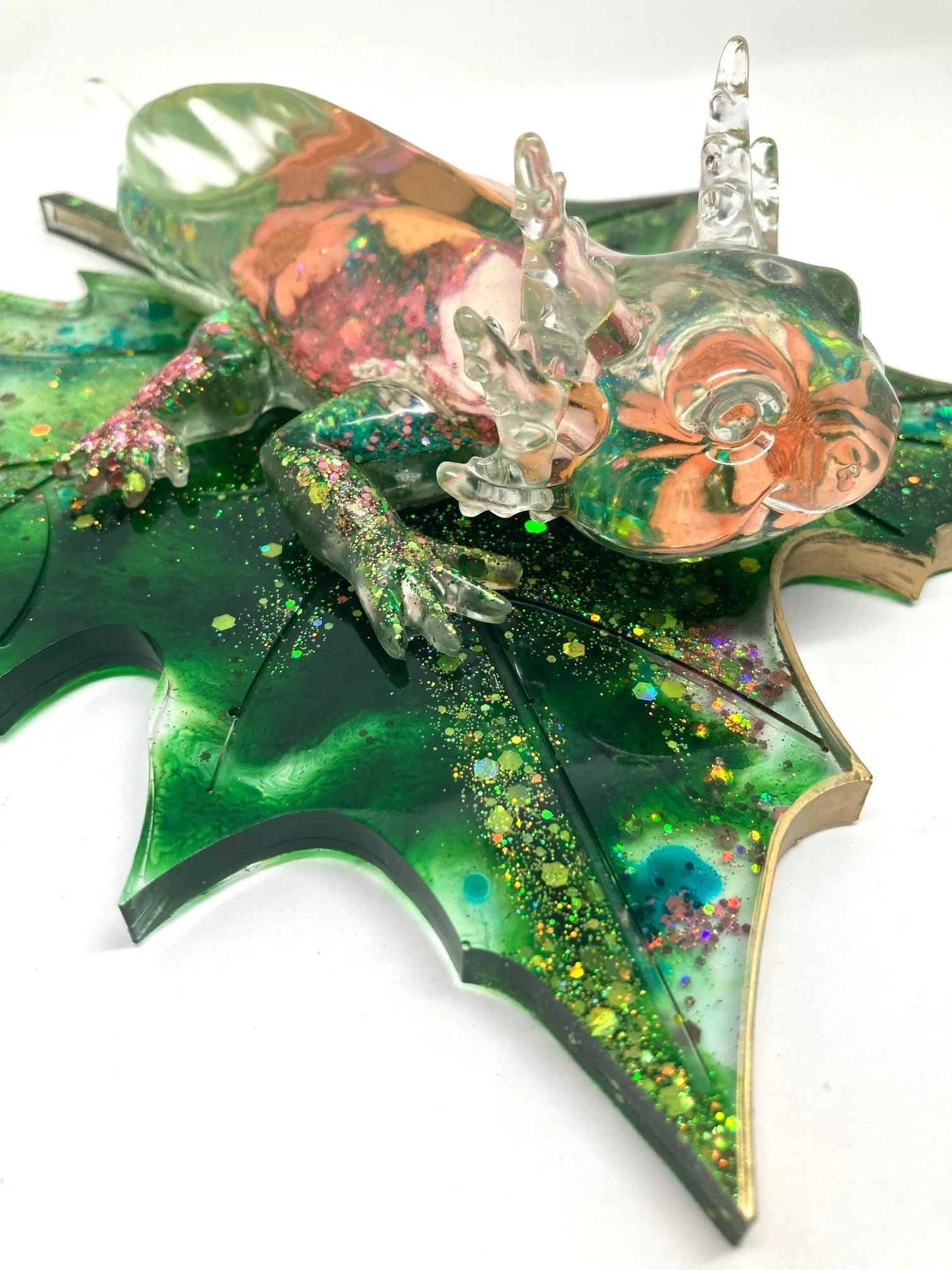 Colorful resin sculpture of a frog perched on a leaf, with iridescent and glitter accents.