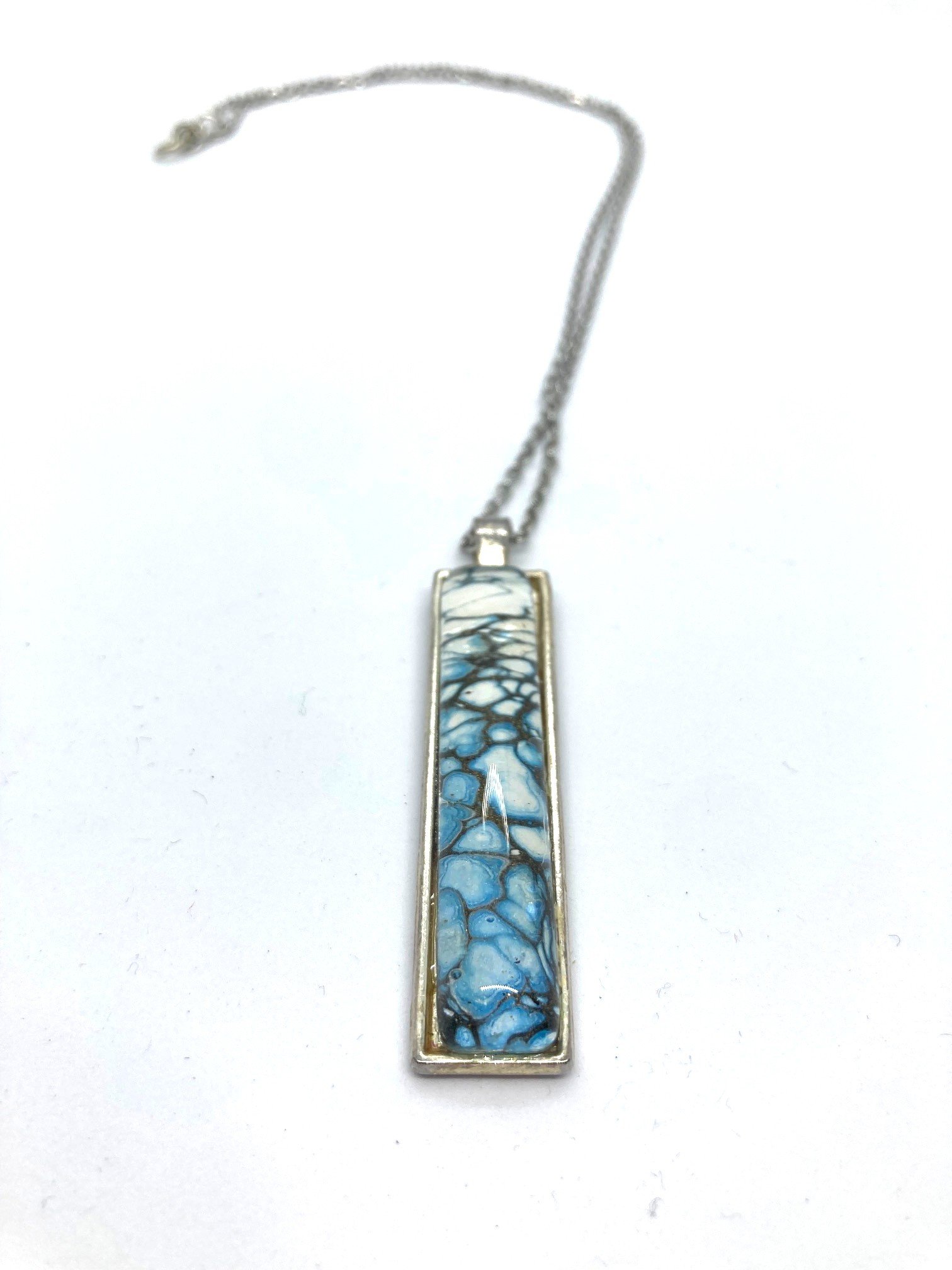 AcrylicPourNecklace_RectangleBezel_BlueandWhiteBubbles_LaidOutCloseup.jpg
