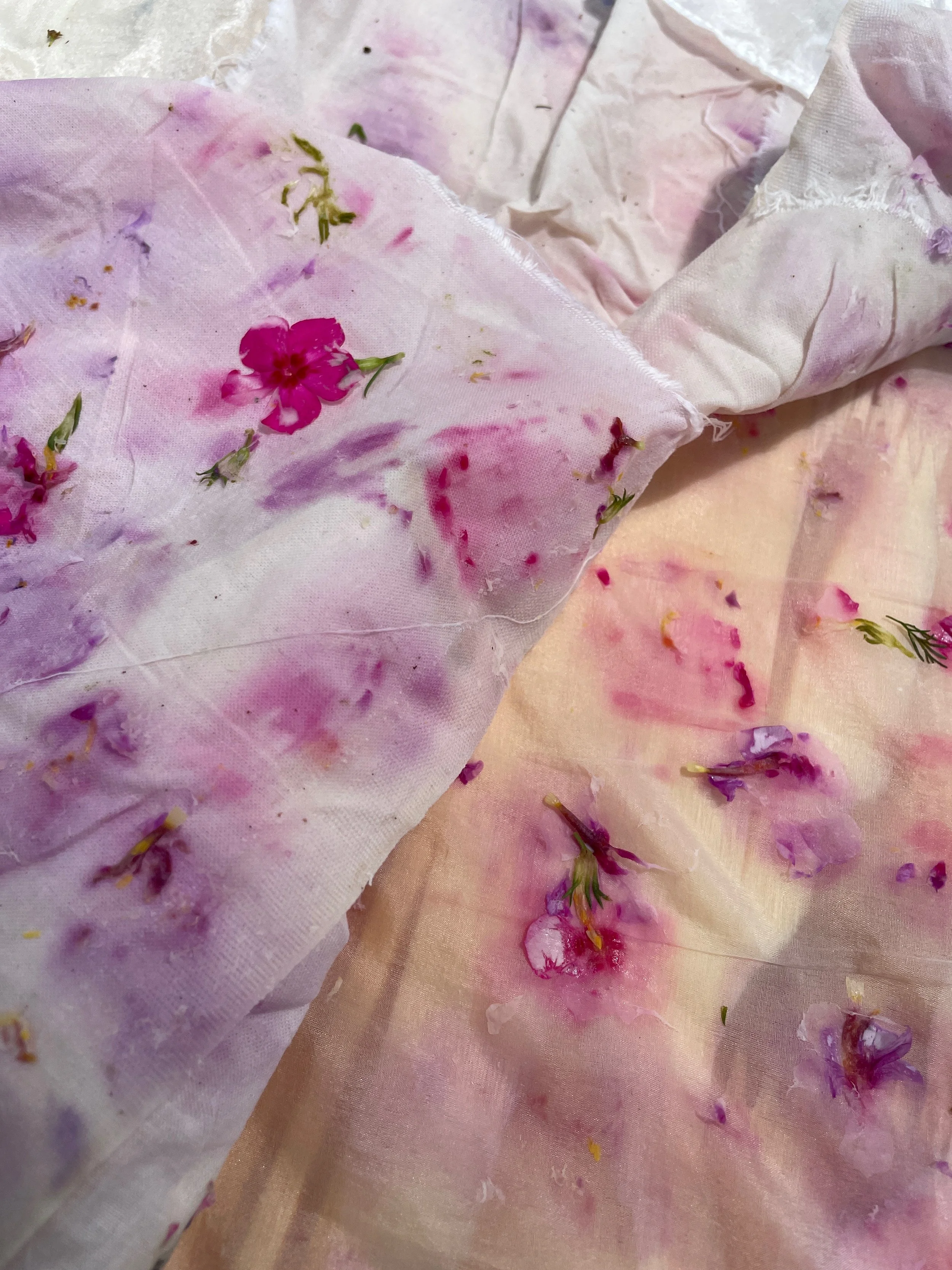 Close-up of watercolor paper with pink, purple, and yellow flower petals and green leaves scattered on it.