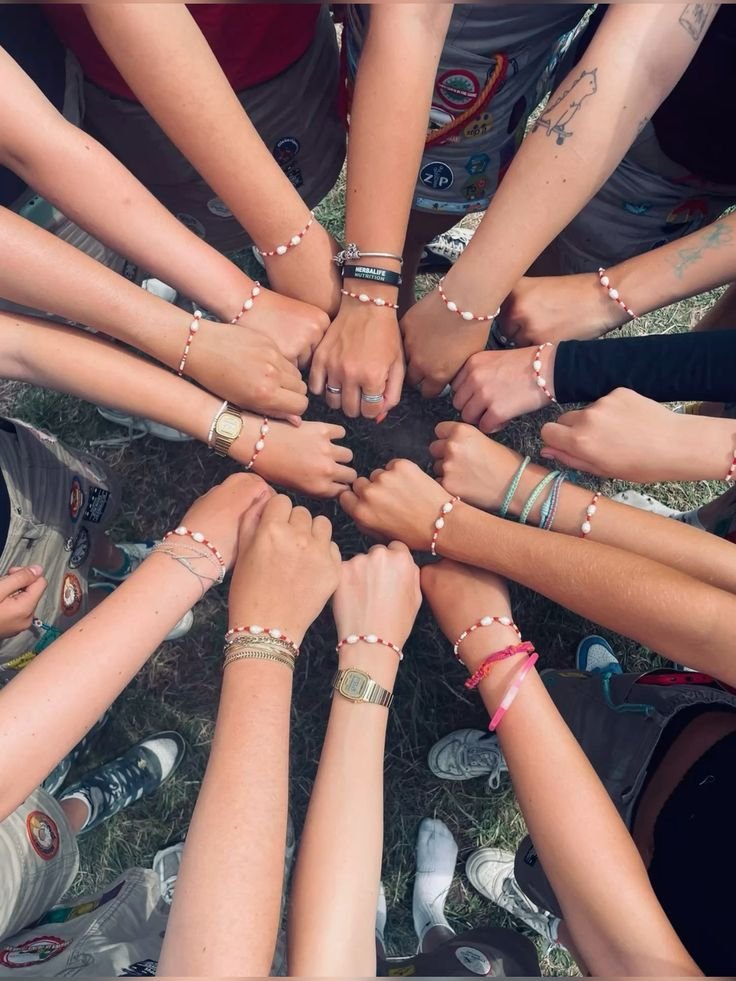 A group of people standing in a circle outdoors, all clasping their fists together in the center. Many are wearing matching beaded bracelets.