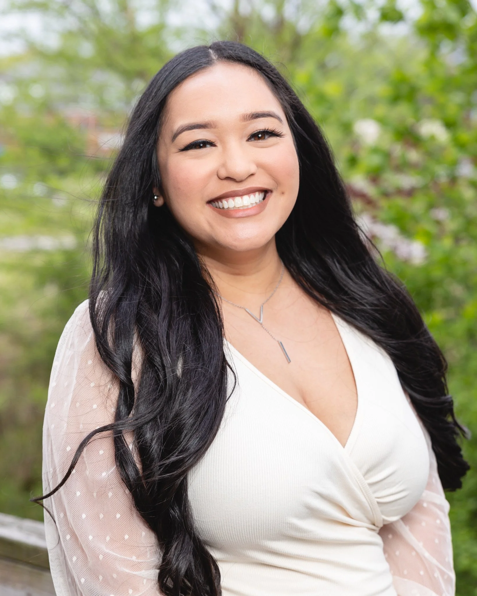 Kaila Laxa, therapist and founder of Transcmend, smiling outdoors in a white top with green trees in the background.