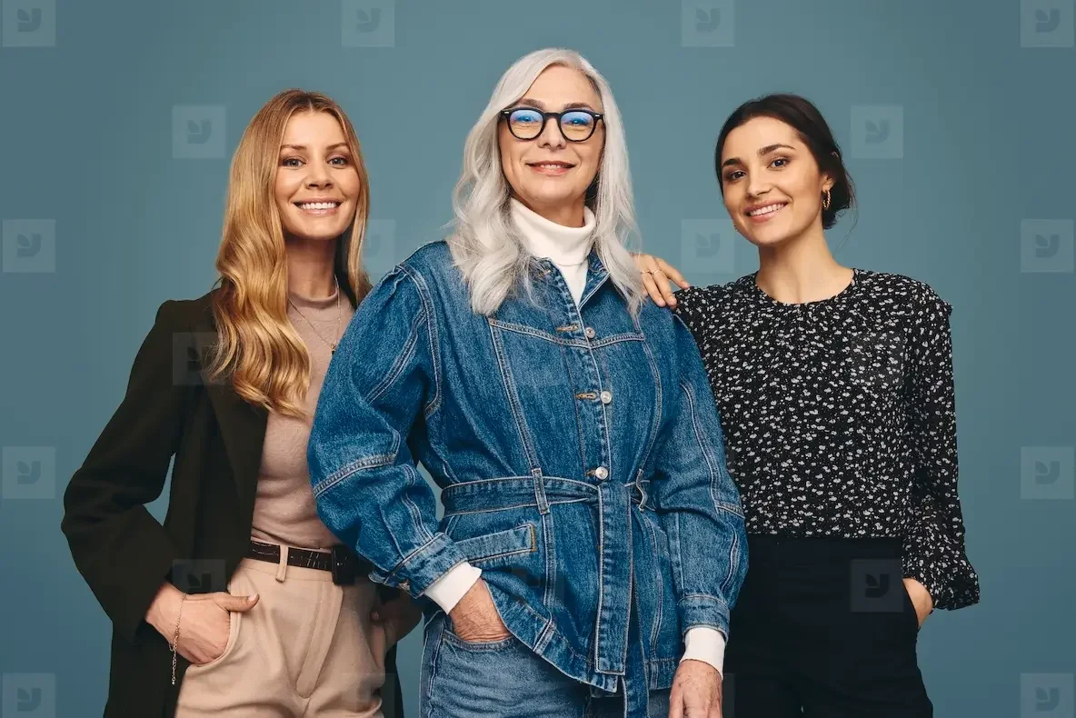 Three women posing together and smiling in front of a blue backdrop, representing the community of women over 40 in the SecondActWomen network.