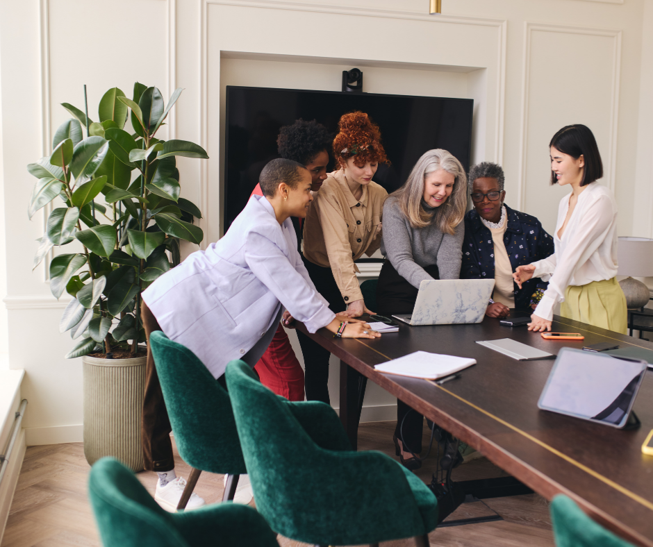 Six professional women collaborating around a conference table, representing the community of women 40 plus leading in work and business.