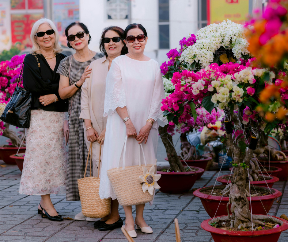 Four stylish midlife women wearing sunglasses standing together outdoors near vibrant flowers, representing friendship and confidence in the SecondActWomen community.