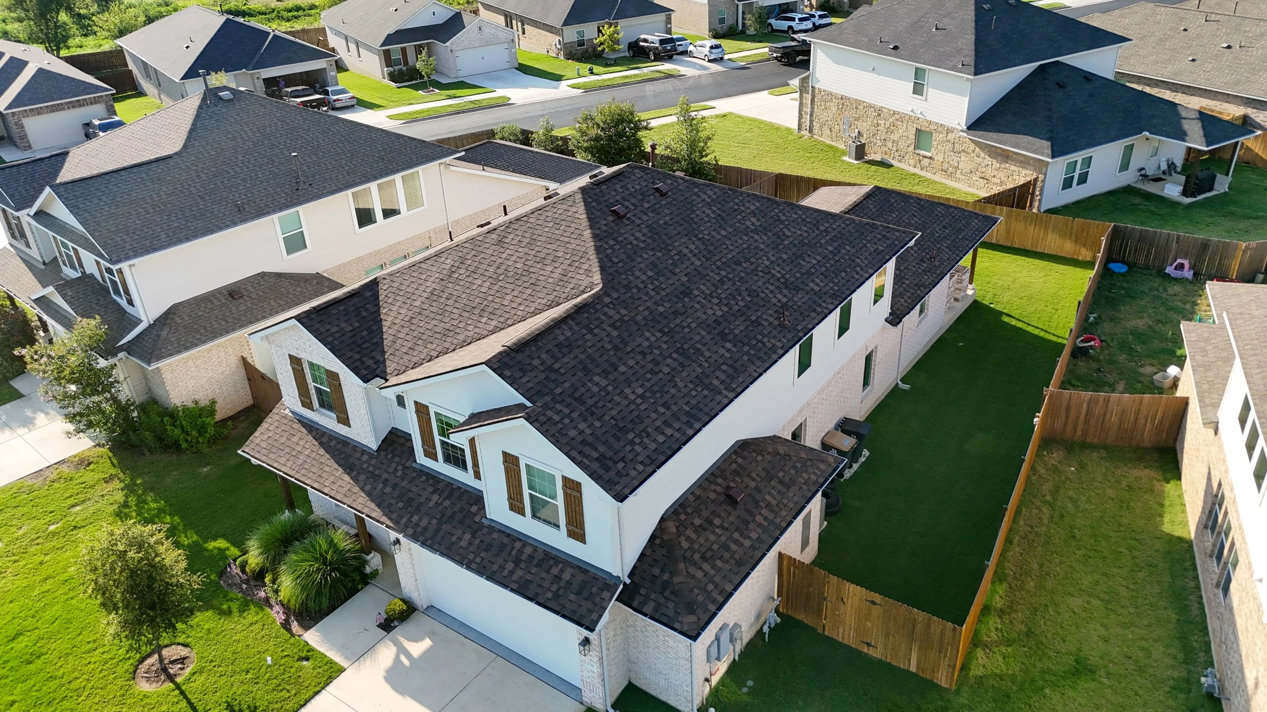 Aerial view of a house with a gray shingle roof, surrounded by trees and a yard with a trampoline.
