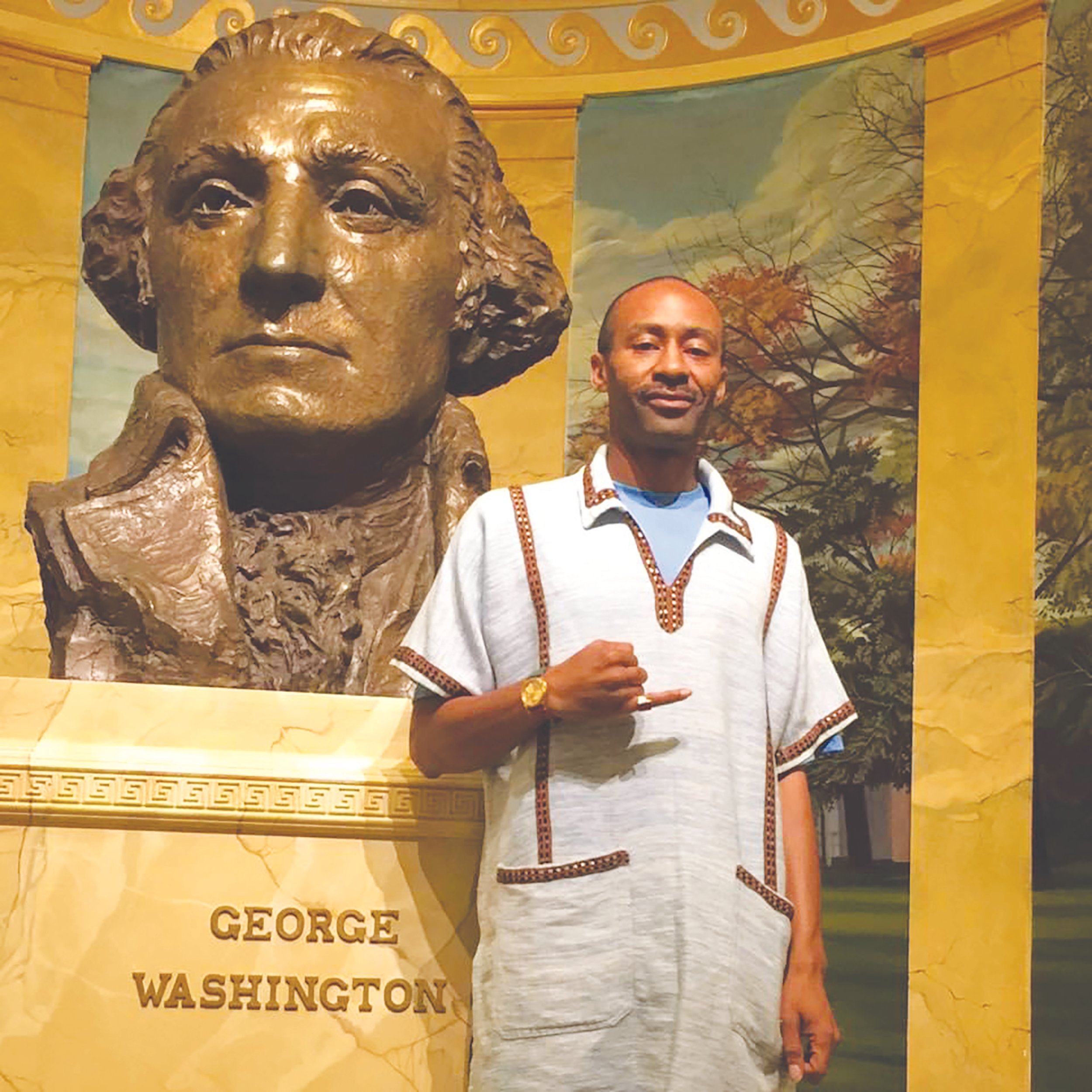 A man standing in front of a large statue of George Washington's head with a painted background of trees and a sky.