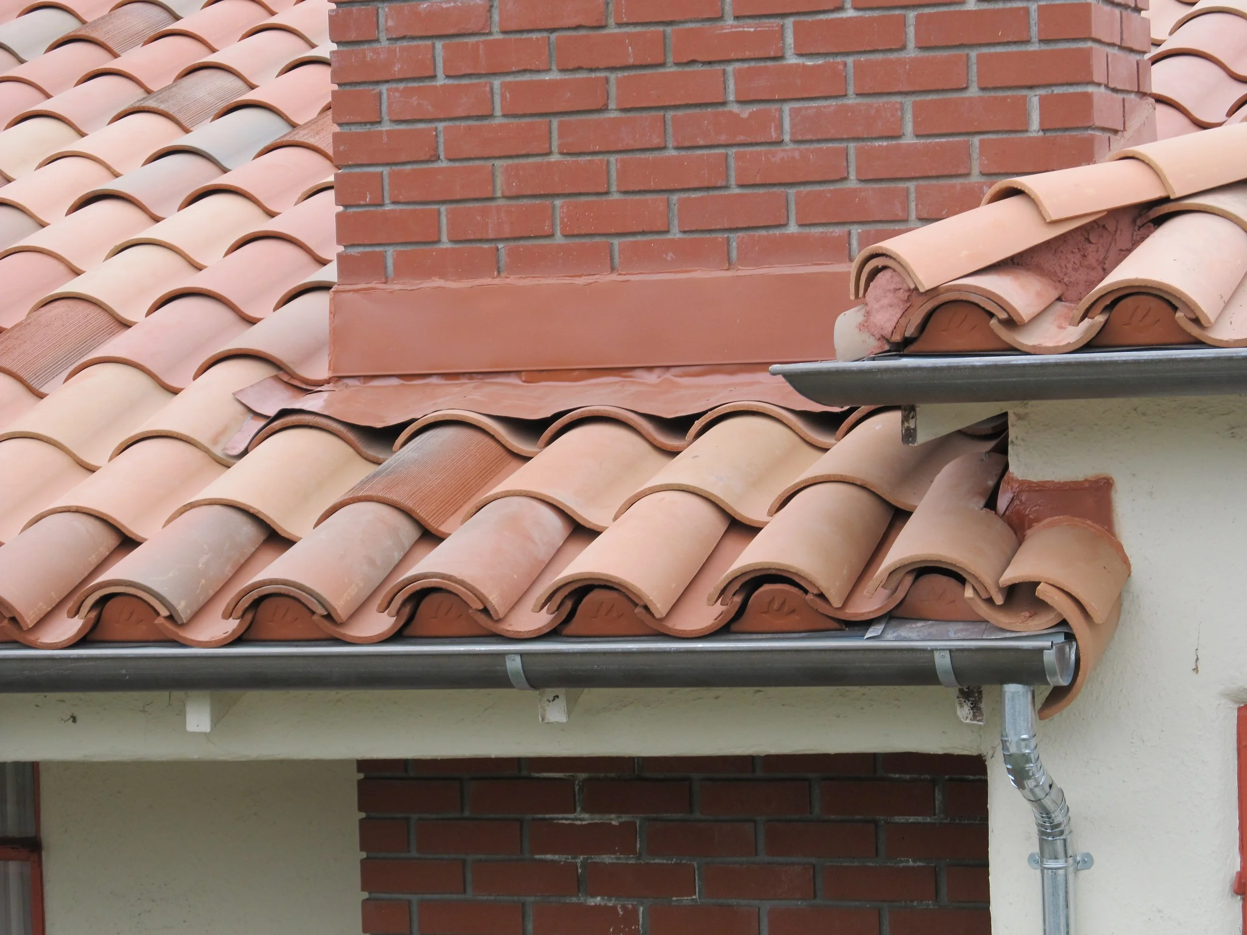 Close-up of a tiled roof with clay tiles, a red brick chimney, and rain gutter system.