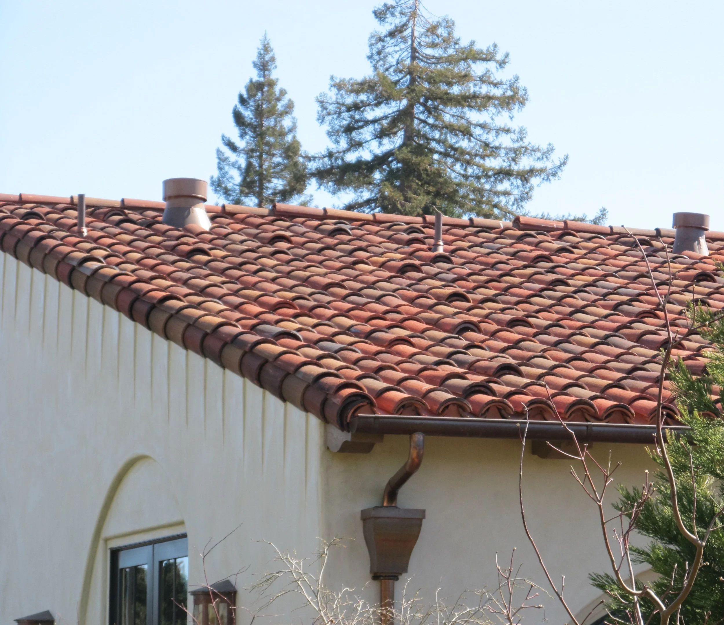 House with red tile roof, window, rain gutter, and trees in background.