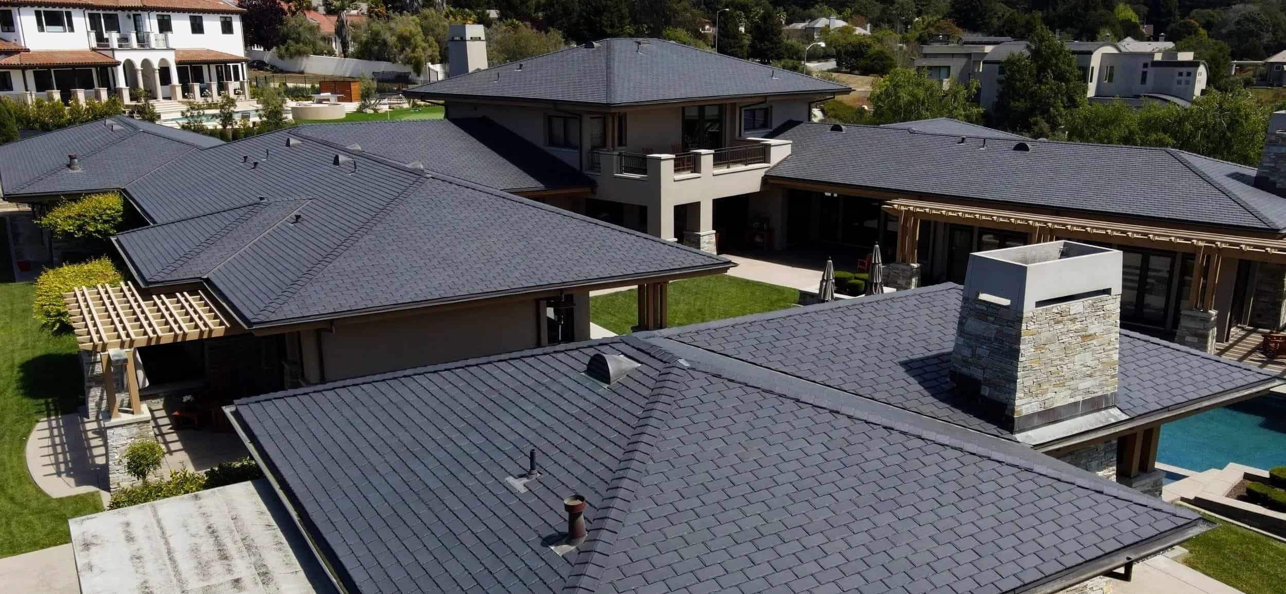 A two-car garage with white wooden doors, black hardware, and arched openings. There are two black outdoor lamps and a driveway made of interlocking bricks. A shrub is on the left side near trash bins under a gray roof.