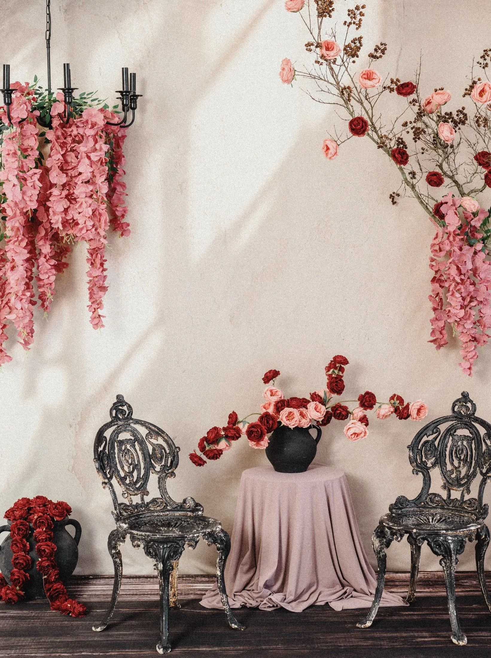 Decorative floral studio setting with pink and red flowers, vintage black chairs, and a small table with a pink cloth and floral arrangement, promoting a creative studio rental event.