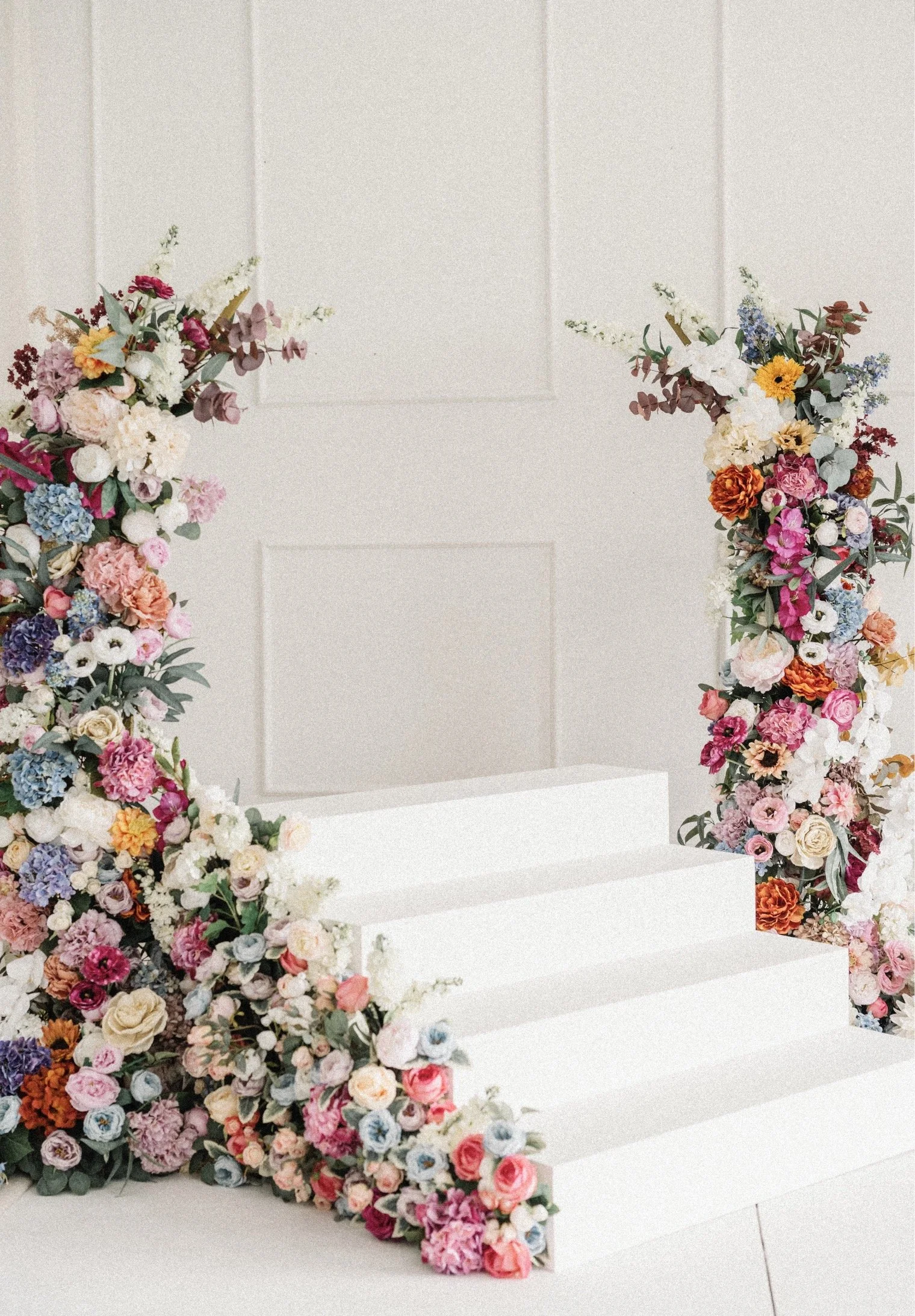 Decorative floral arrangement with pink, purple, white, and green flowers on white stairs, promoting an event from March 5th to May 4th.