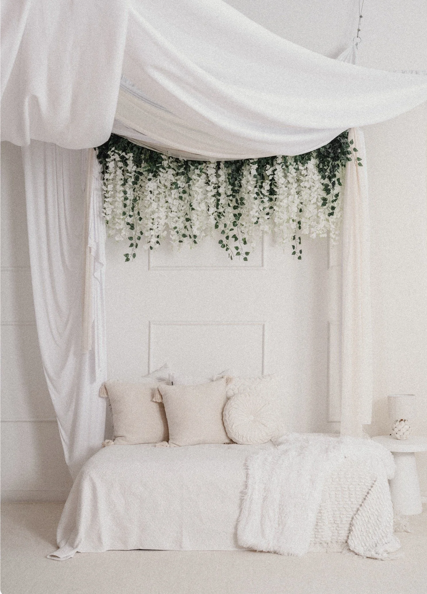 Elegant bedroom with white bed, decorative pillows, and floral canopy with white flowers and greenery.