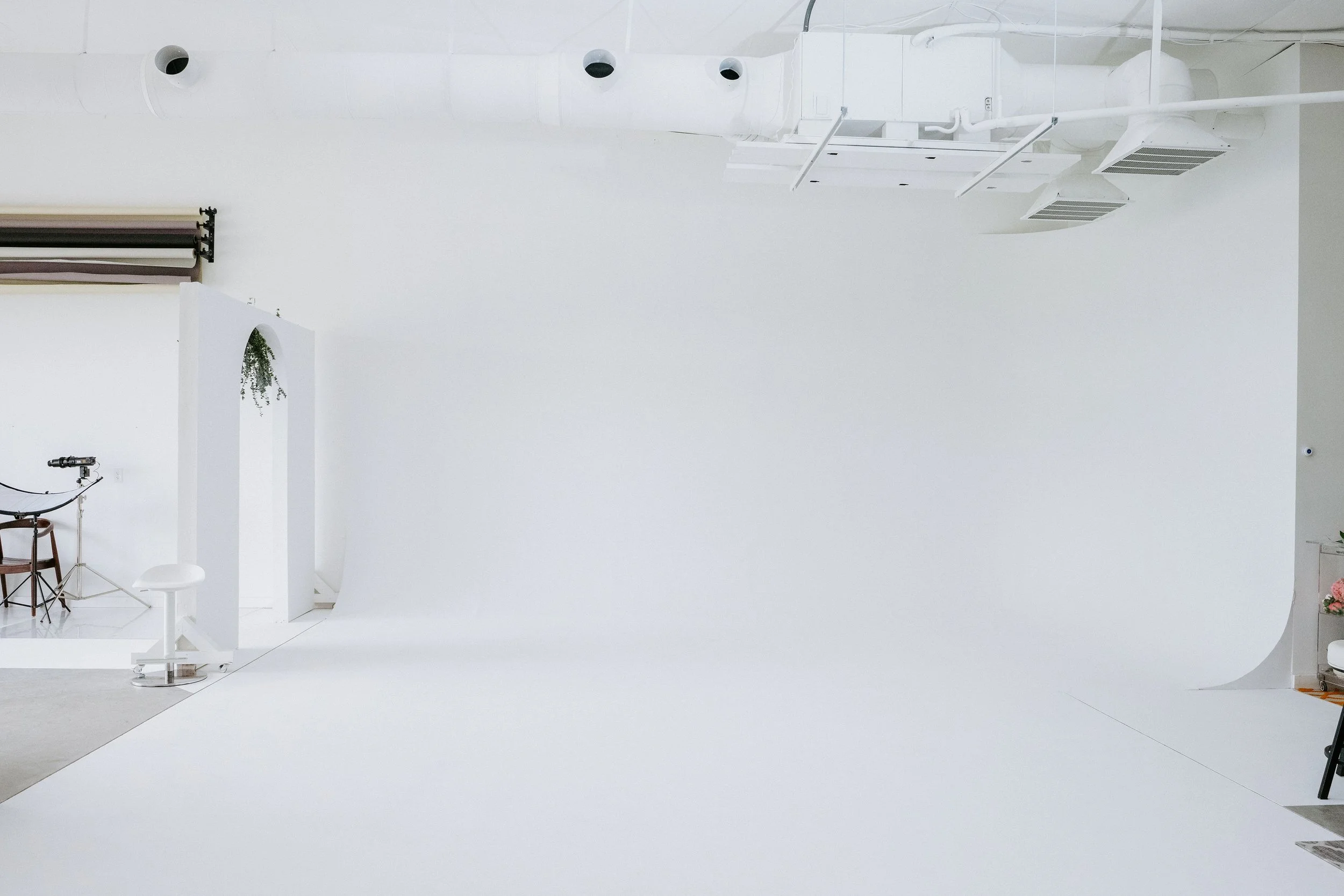 Empty white photography studio with a seamless white backdrop, studio equipment, and minimal furniture.