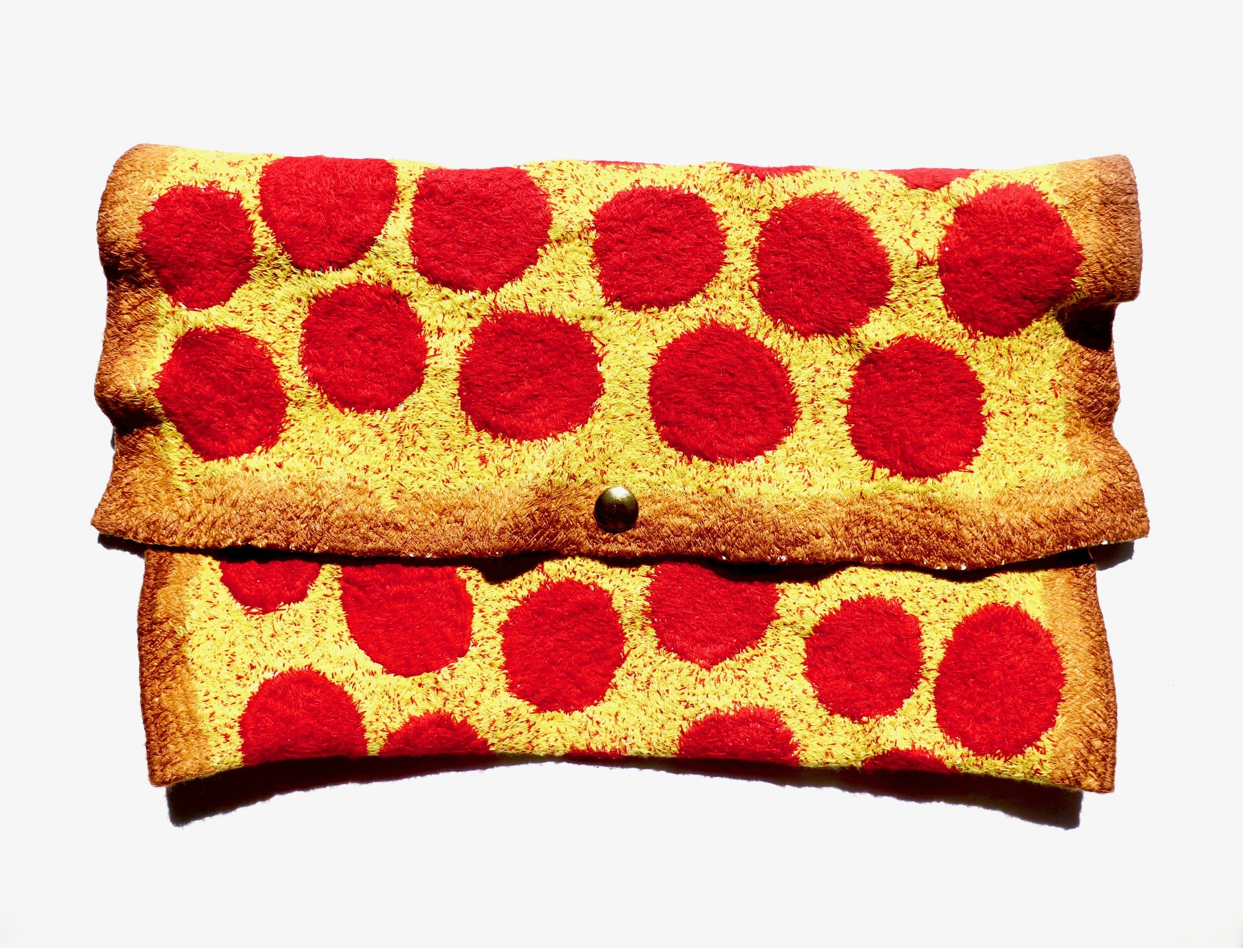 Rectangular embroidered pizza clutch with a yellow surface, raised red pepperoni circles, golden-brown crust, and brass-tone closure.
