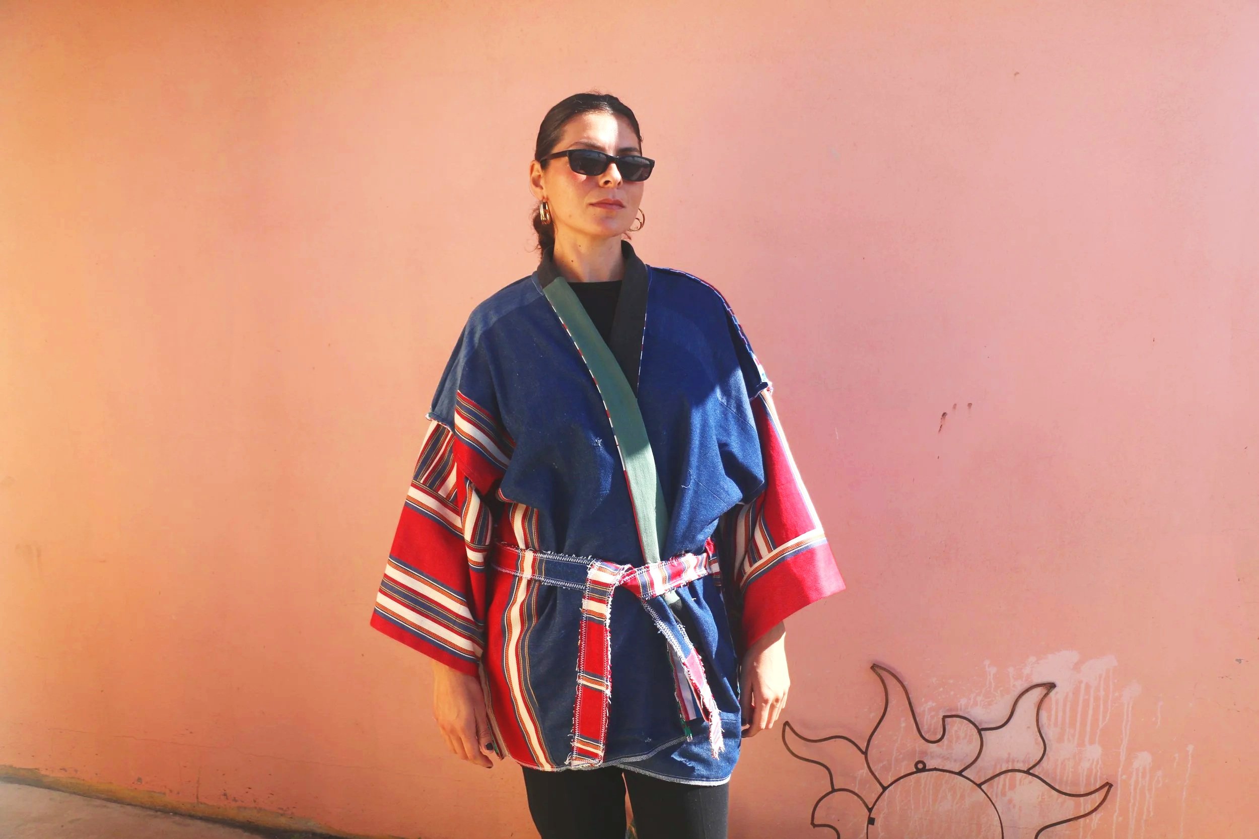 A model wearing a reversible blue denim kimono with red, white, and blue striped panels, contrasting green trim, and a coordinating fabric belt.