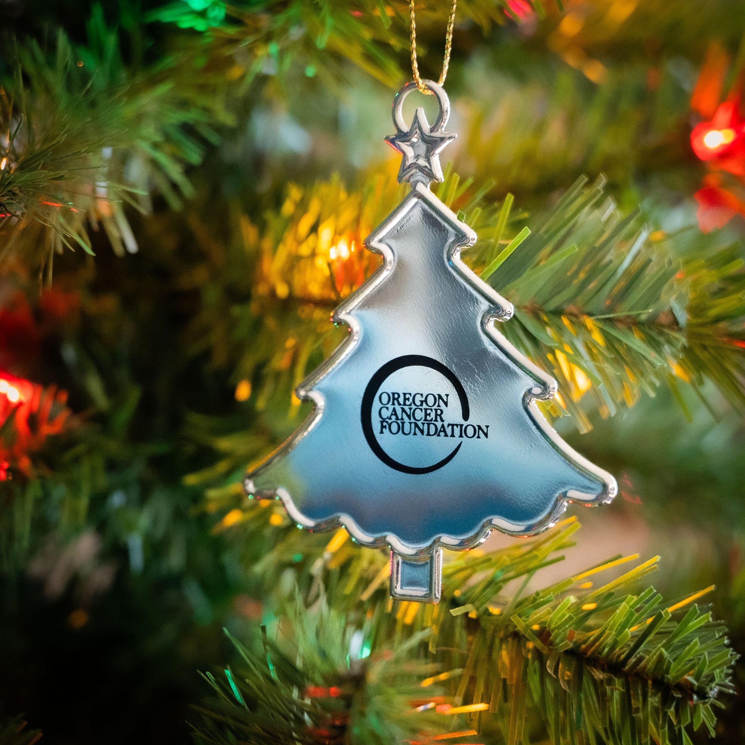 A silver tree-shaped ornament with the Oregon Cancer Foundation logo printed in black