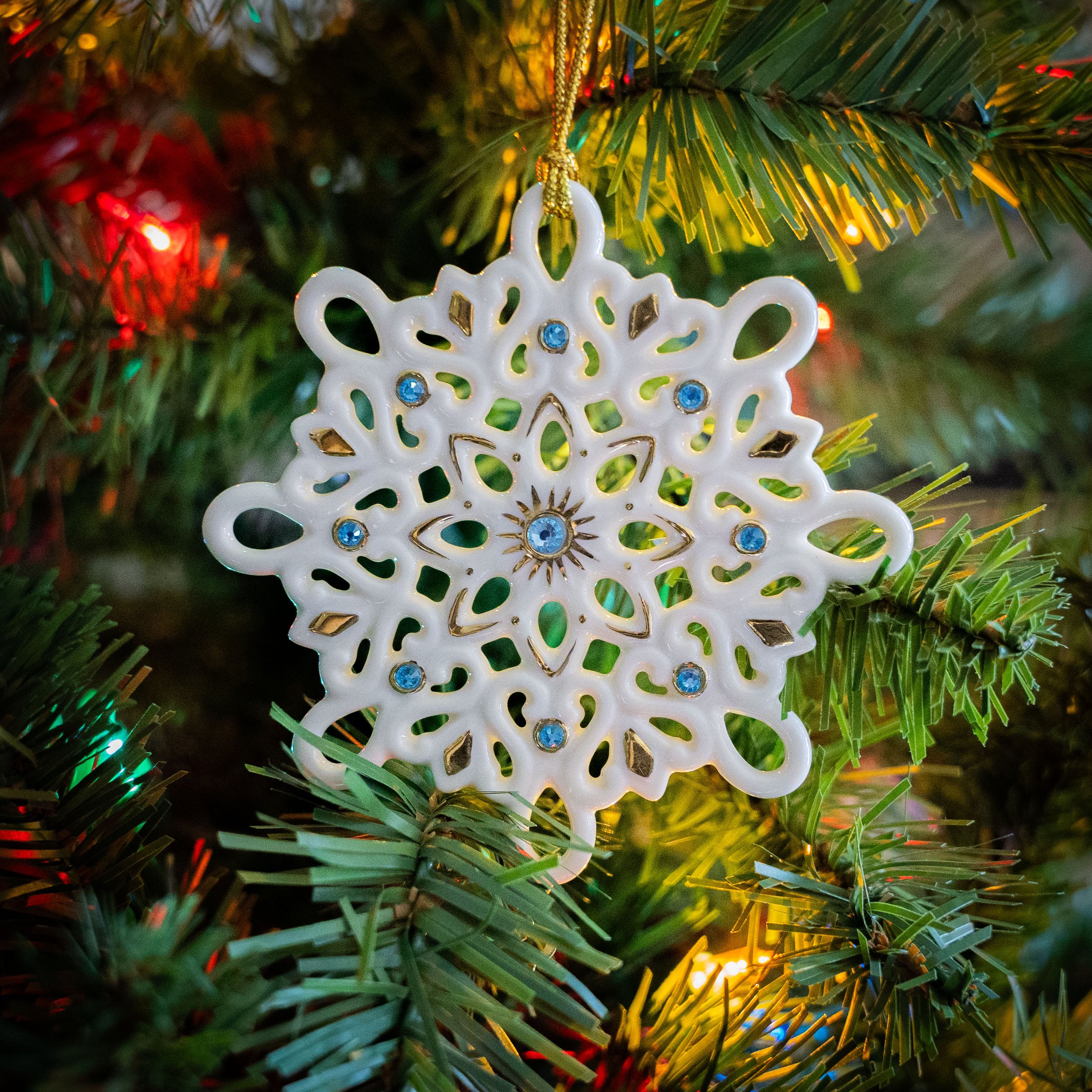 A white porcelain snowflake ornament with gold details and blue gems