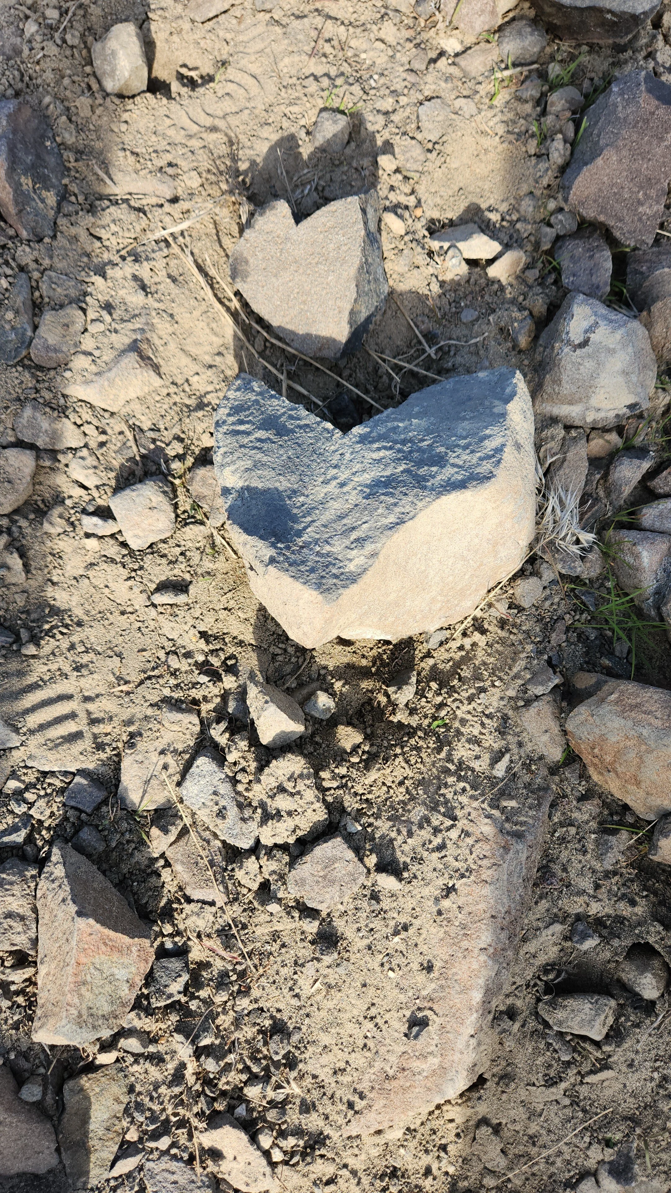 Three rocks arranged to resemble a heart shape on dirt and gravel ground.