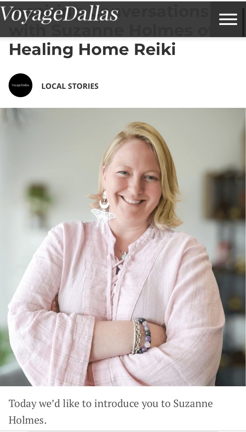 A smiling woman with blonde hair wearing a light pink blouse, large earrings, a bracelet, and a necklace in a softly blurred indoor setting.