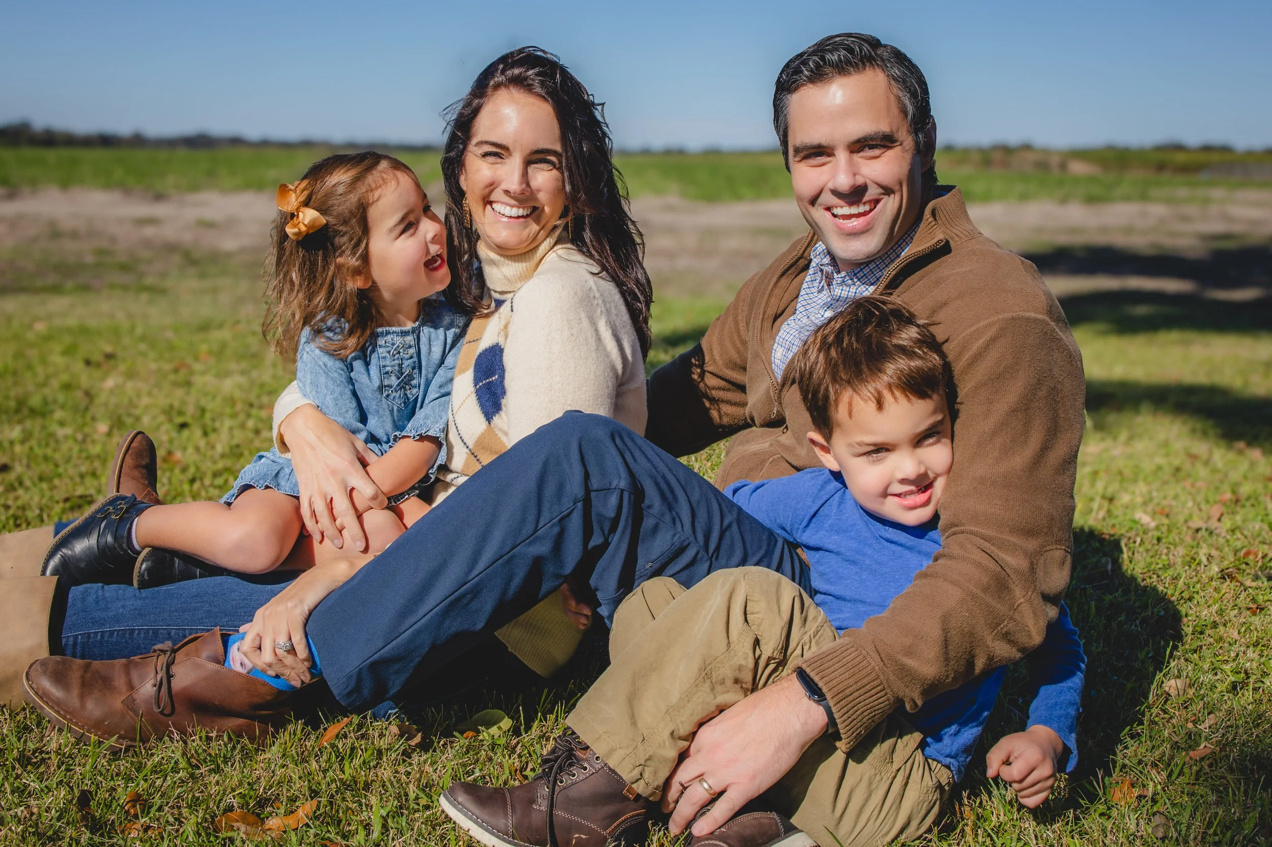 Family sitting on grass outdoors with blue sky, smiling and enjoying the day