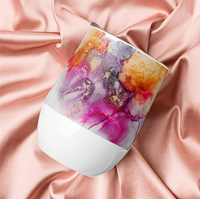 A colorful, abstract design on a glass tumbler placed on pink fabric.