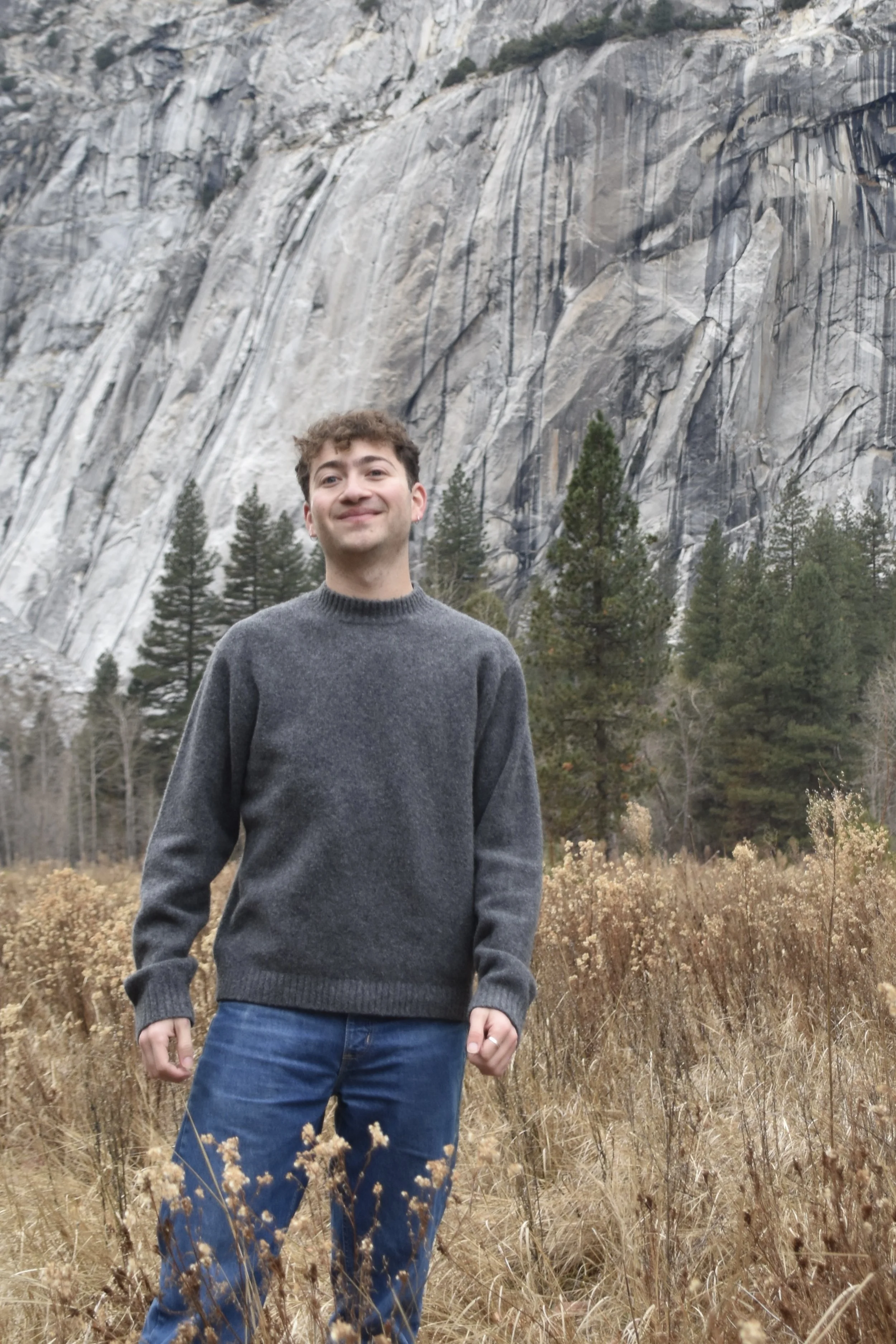 Image of a man with short curly brown hair wearing a dark gray sweater outdoors