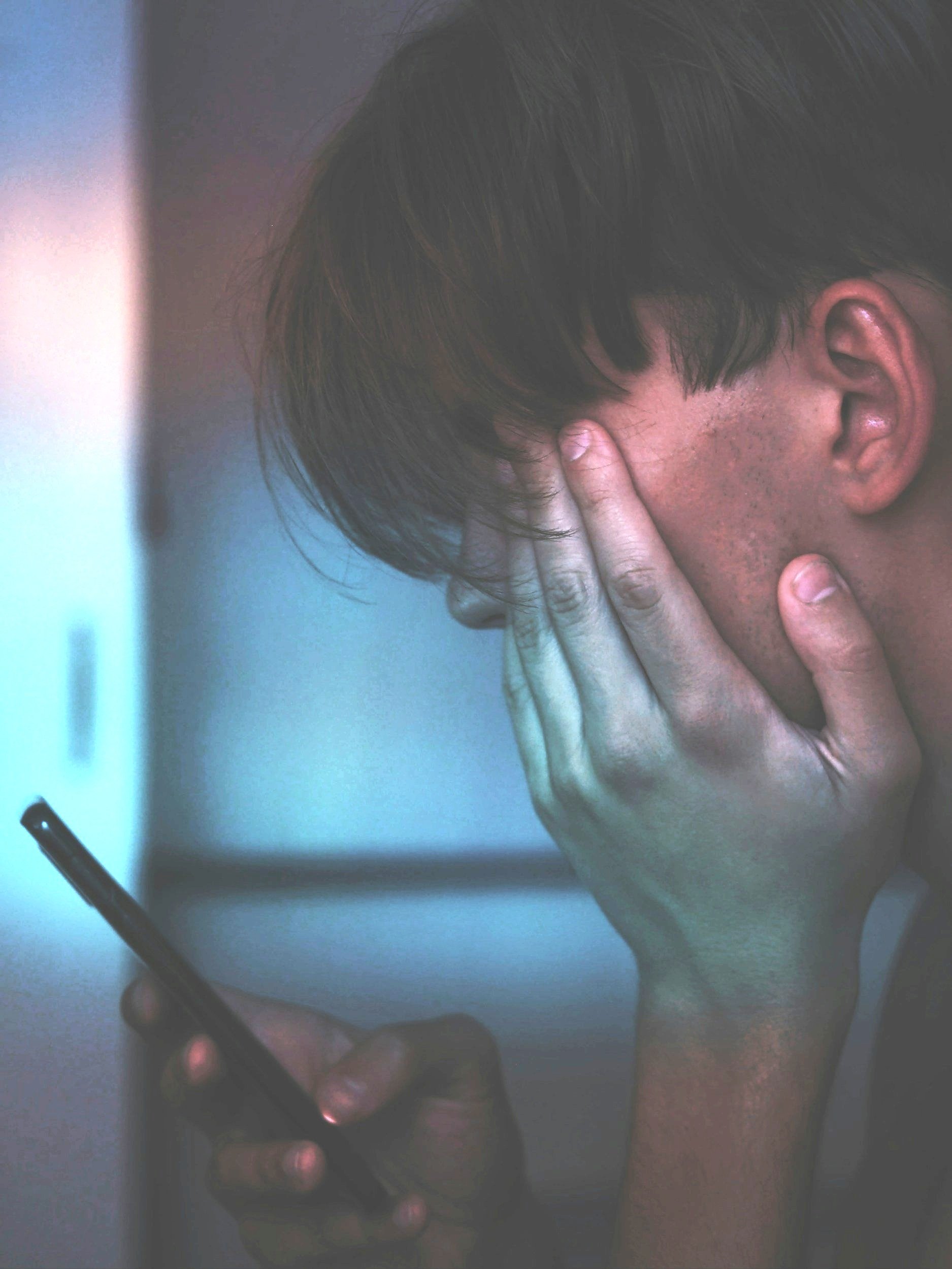 Person holding a smartphone and touching their face in a close-up view.