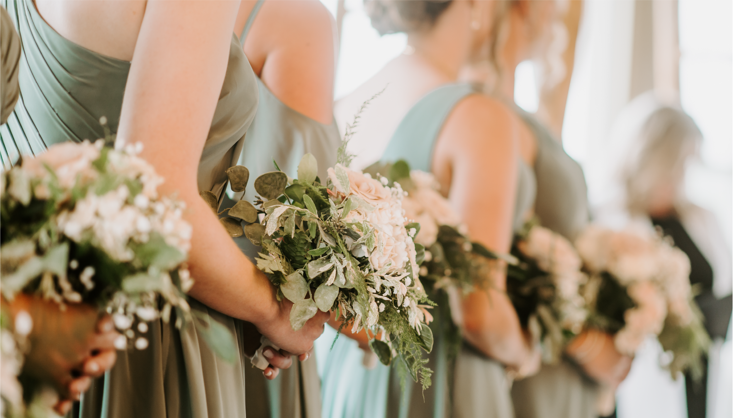 Line of bridesmaids holding floral bouquets, wearing green dresses.