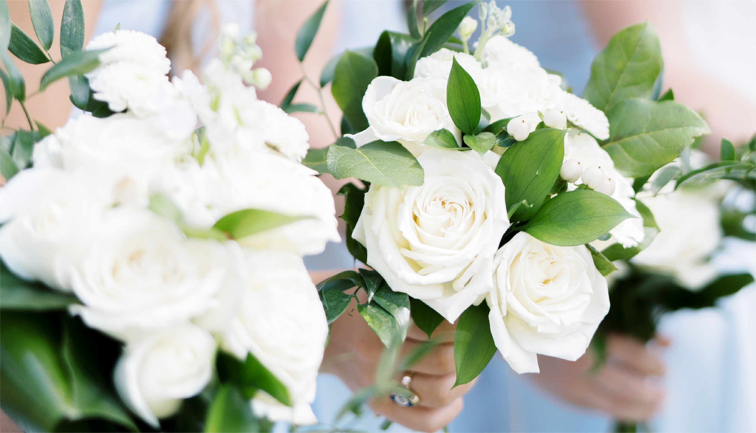 White rose bouquets with greenery held by individuals.