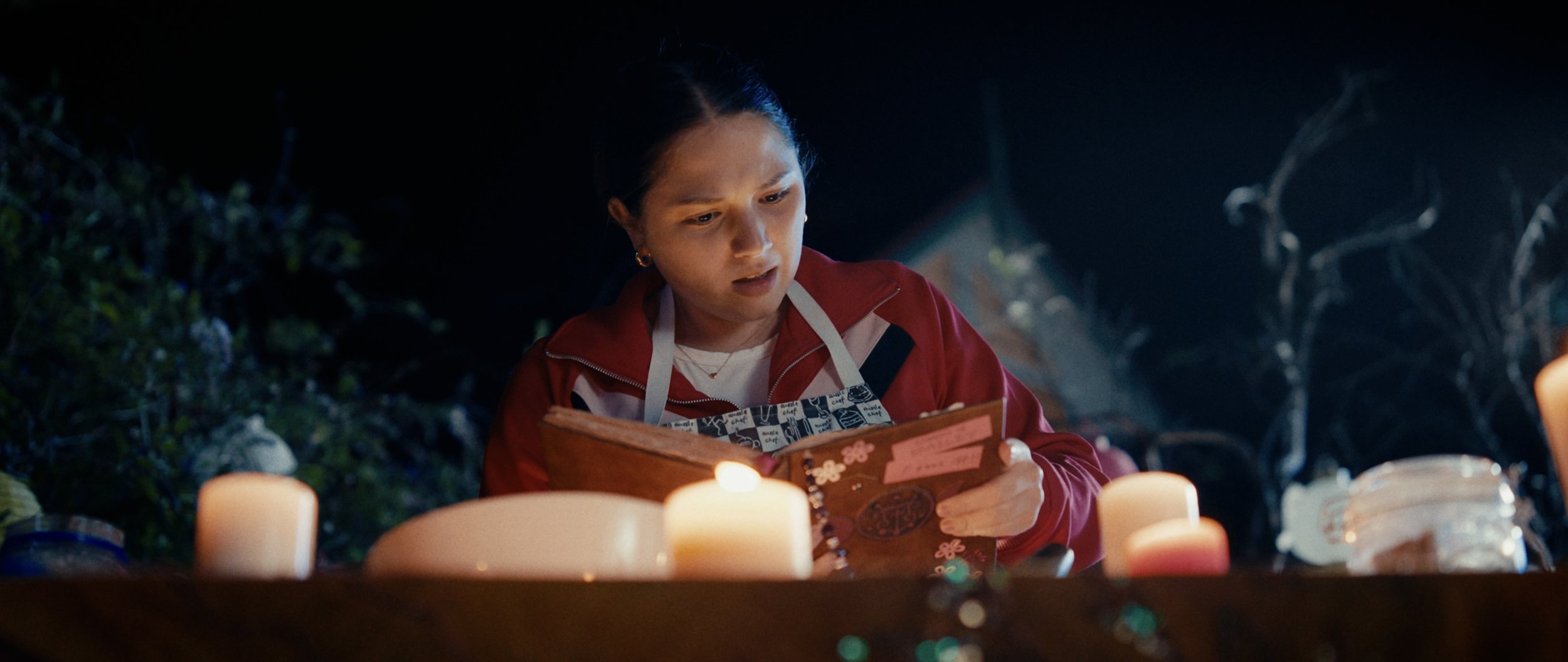 Young woman reading a book at night surrounded by candles and outdoor scenery.