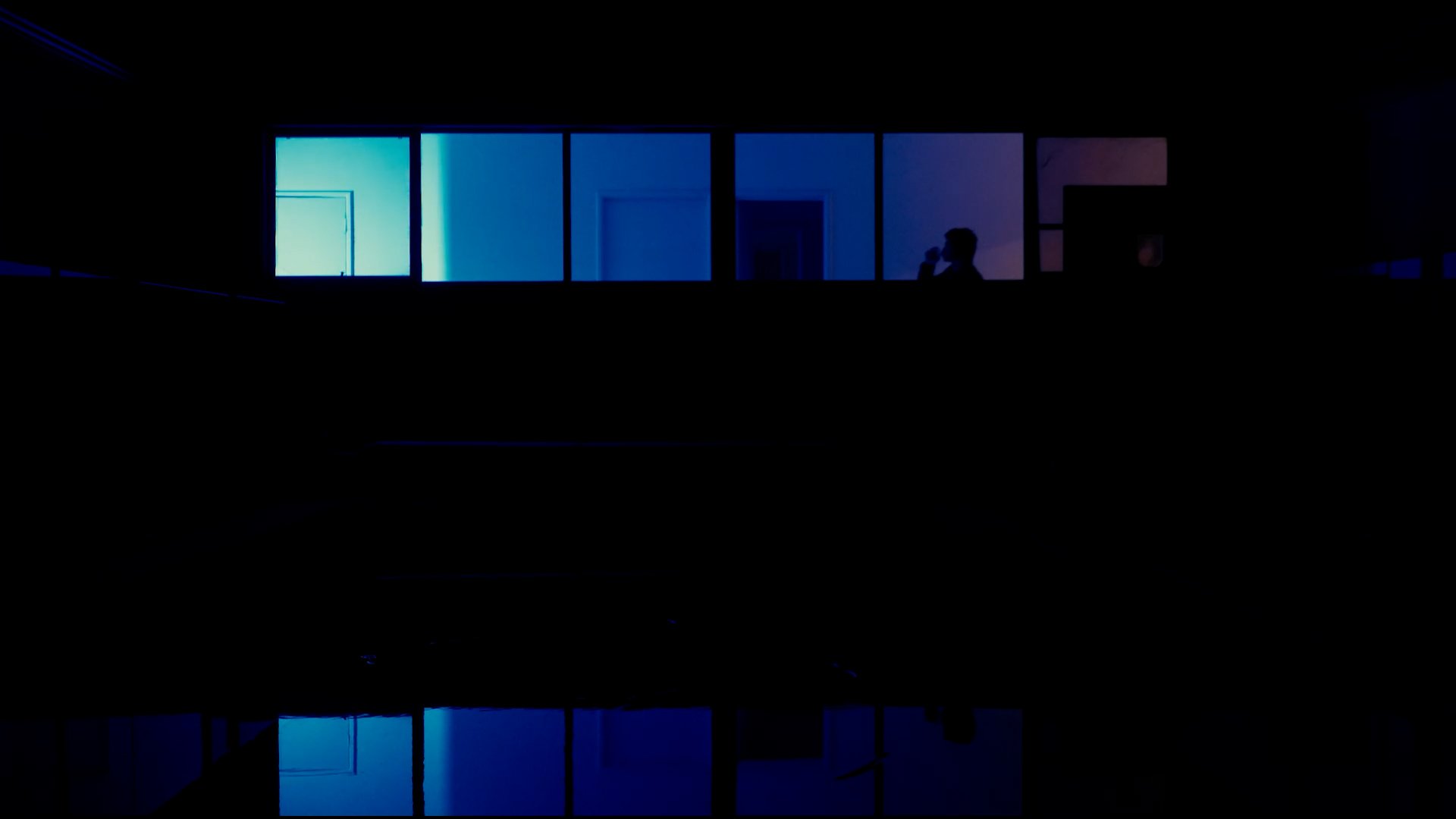 A silhouette of a person holding a drink, standing by a window at night with blue and purple lighting